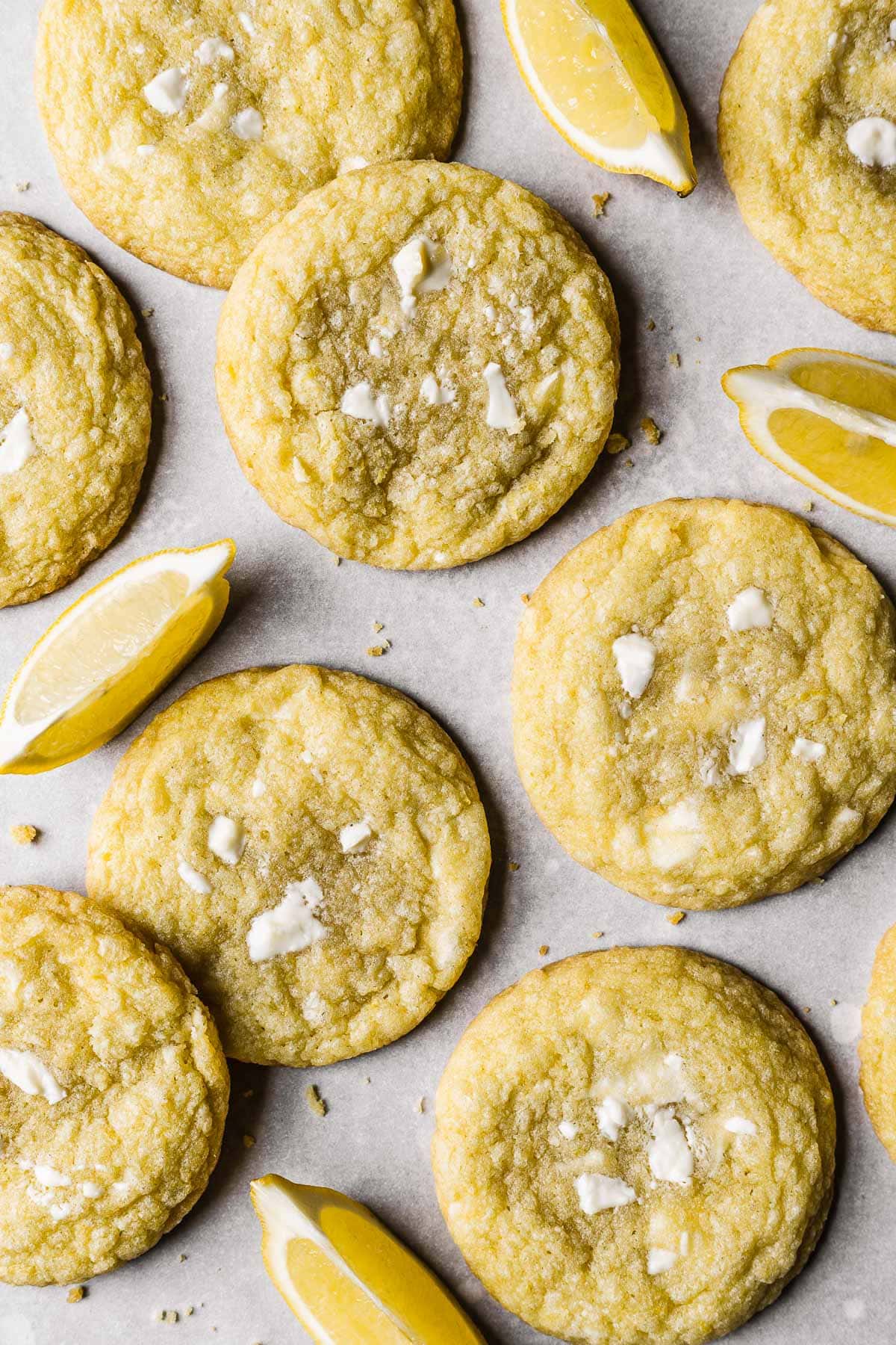 Lemon white chocolate cookies with lemon slices in between on white parchment paper.