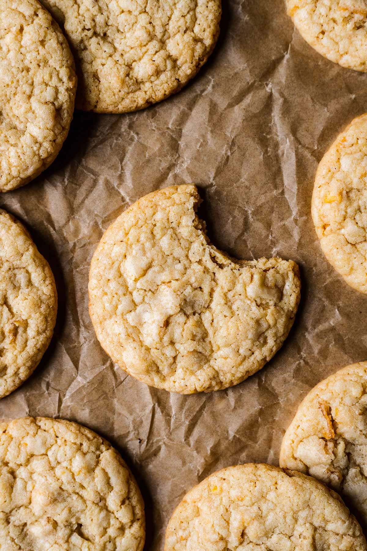 A cookie on brown parchmenet with one bite taken out of it. More cookies peek into the frame.