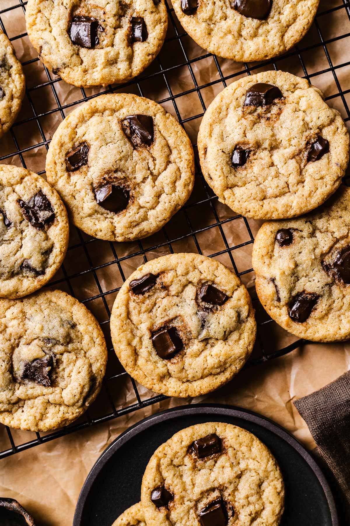 Chocolate chip cookies on a black wire cooling rack with a plate of cookies nearby.