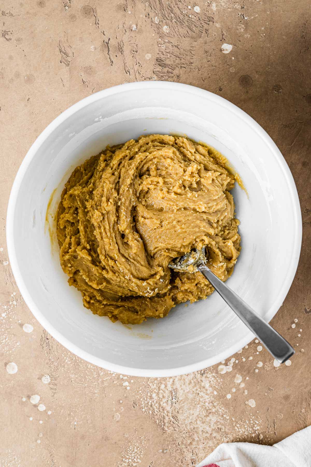 A white mixing bowl with flour added to wet ingredients for blondie dough.