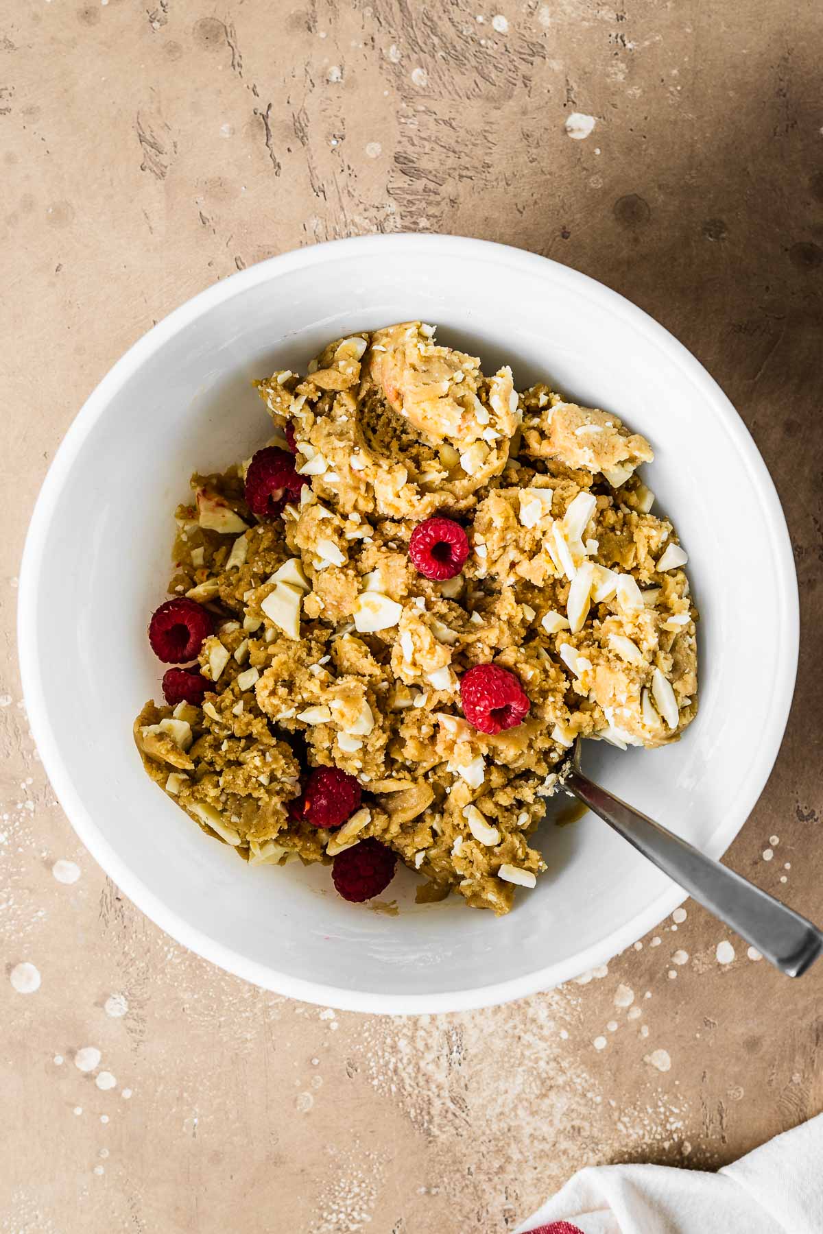 Raspberry and white chocolate blondie dough in a white ceramic mixing bowl.