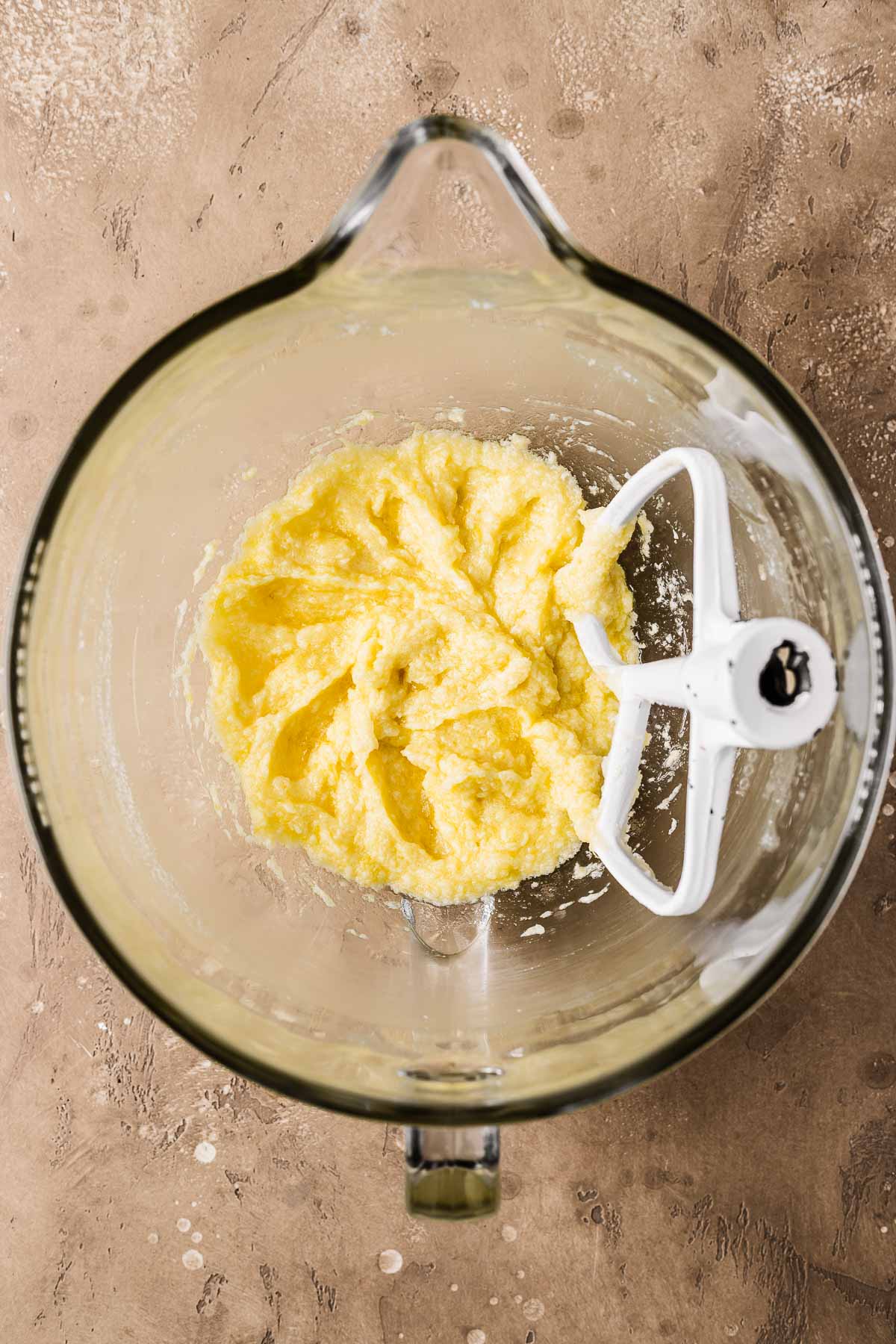 A clear glass mixing bowl with butter, sugar and eggs mixed together.