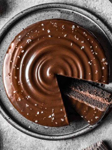 A chocolate ganache covered chocolate cake with a slice cut out and turned on an angle to show the inside.