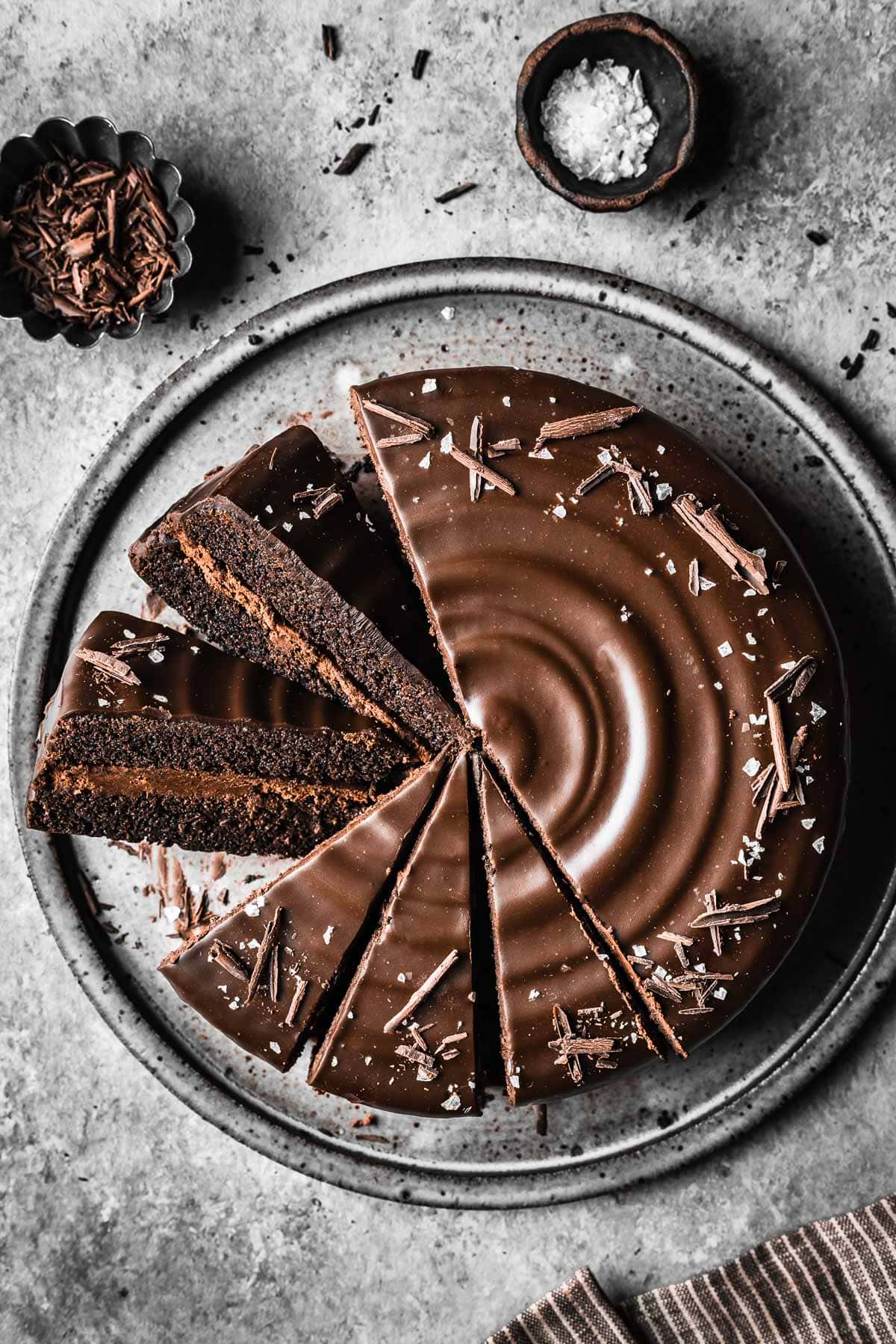 A chocolate ganache cake on a grey ceramic plate with two slices turned on an angle to show the whipped chocolate ganache filling.