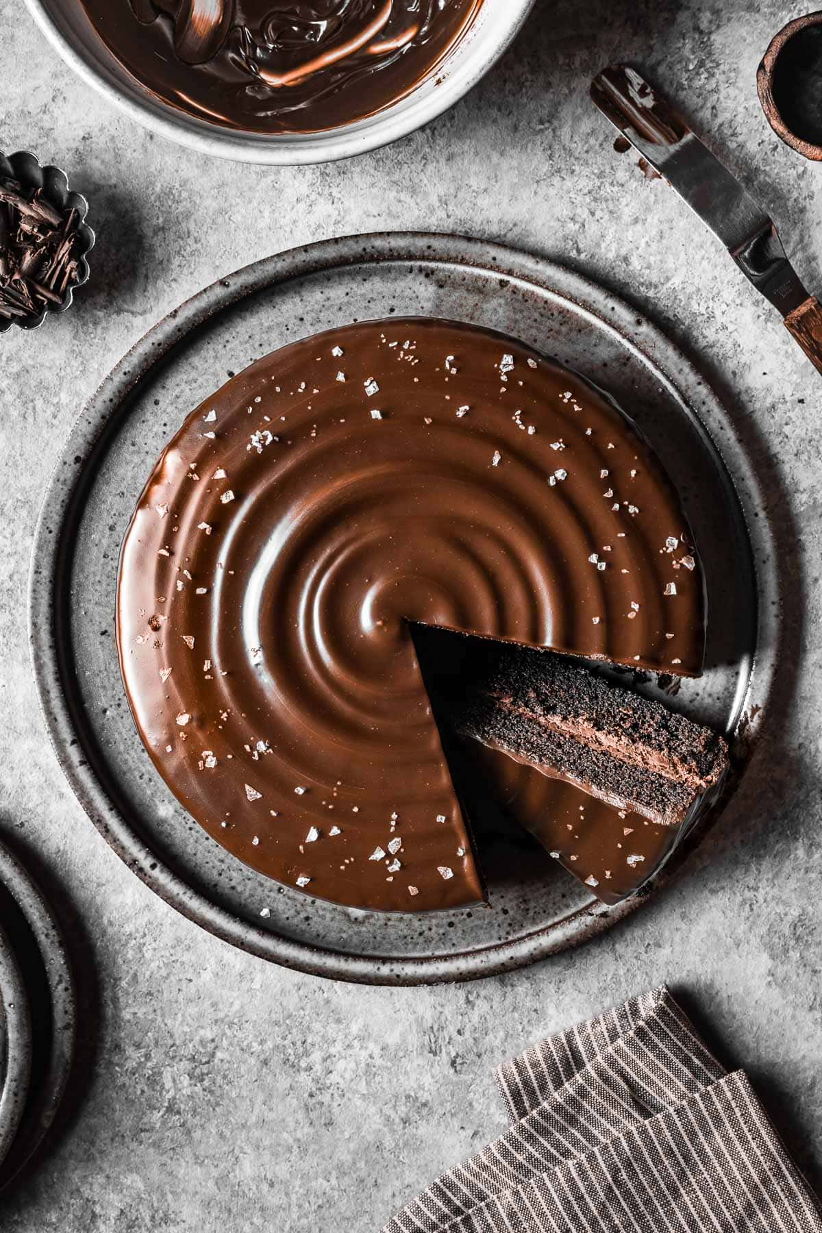 A chocolate ganache covered chocolate cake with a slice cut out and turned on an angle to show the inside.