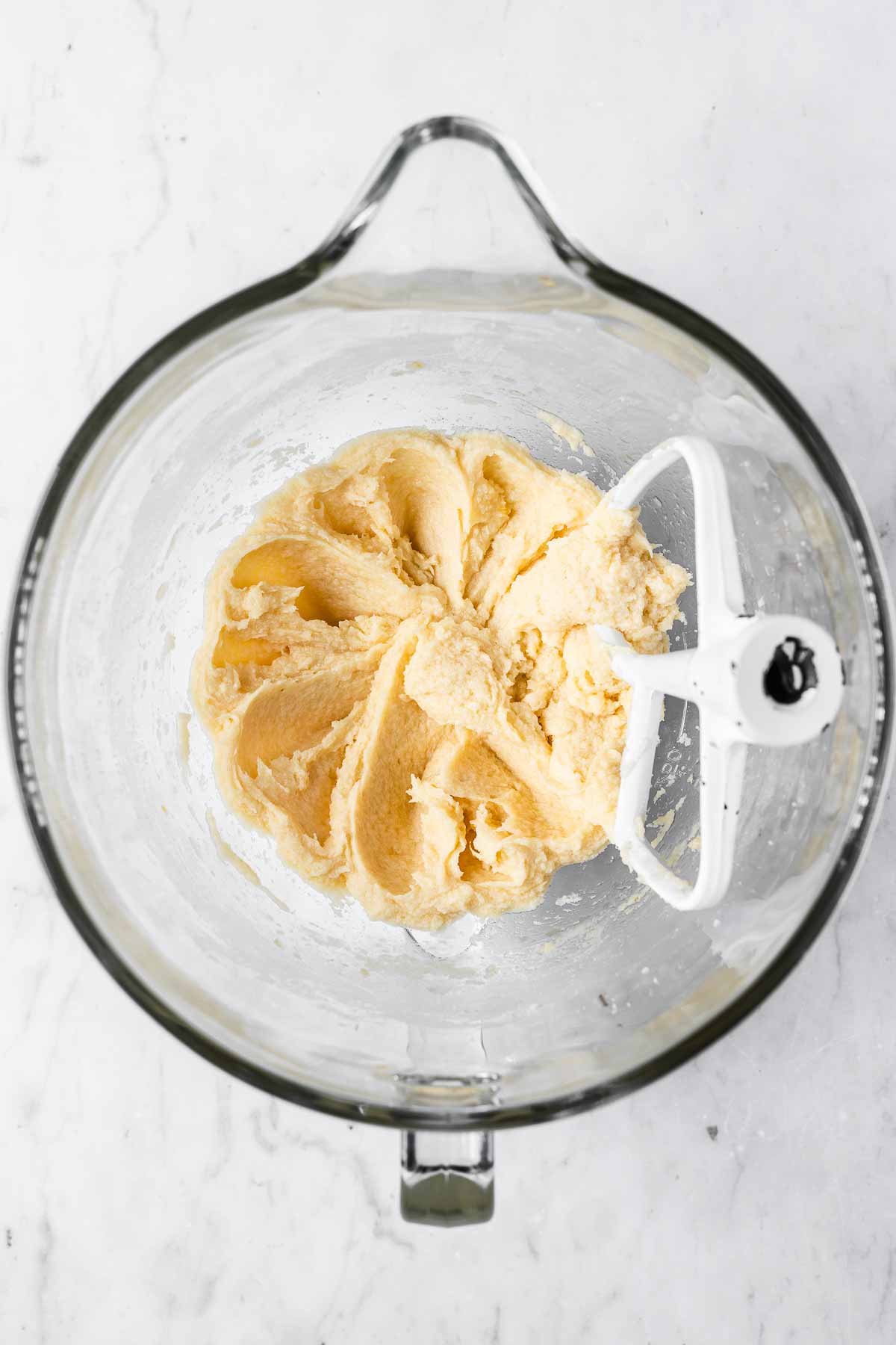 A clear glass mixing bowl with creamed butter, sugar, and eggs added.