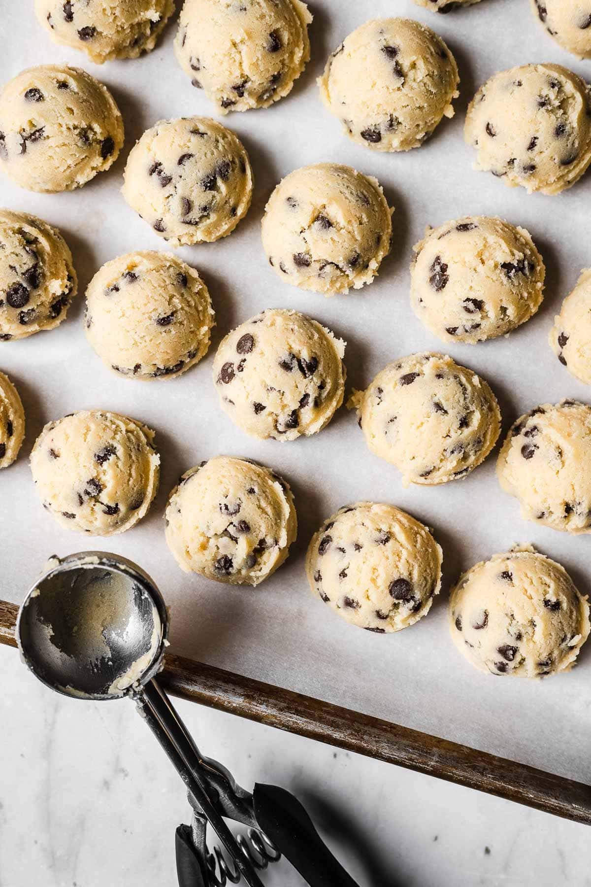 Scoops of chocolate chip cookie dough without brown sugar on a white parchment paper lined cookie sheet.