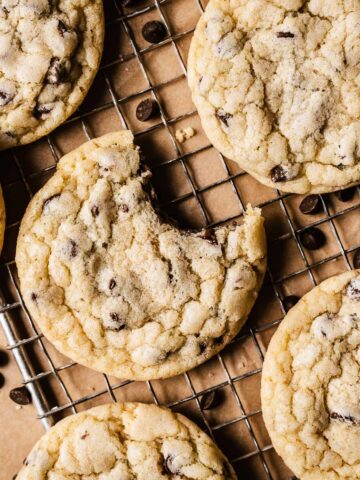 Chocolate chip cookies on a wire cooling rack with one bite taken out of a cookie.