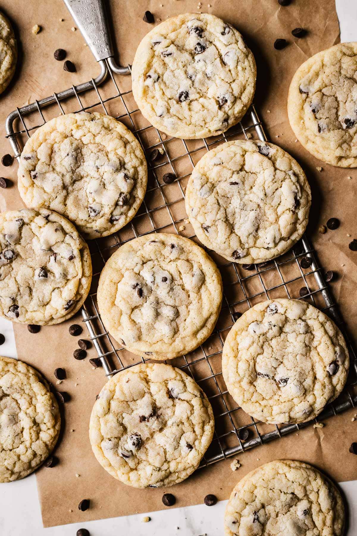 Cookies on a wire cooling rack with brown parchment paper underneath. There are chocolate chips and cookie crumbs sprinkled around the cookies.