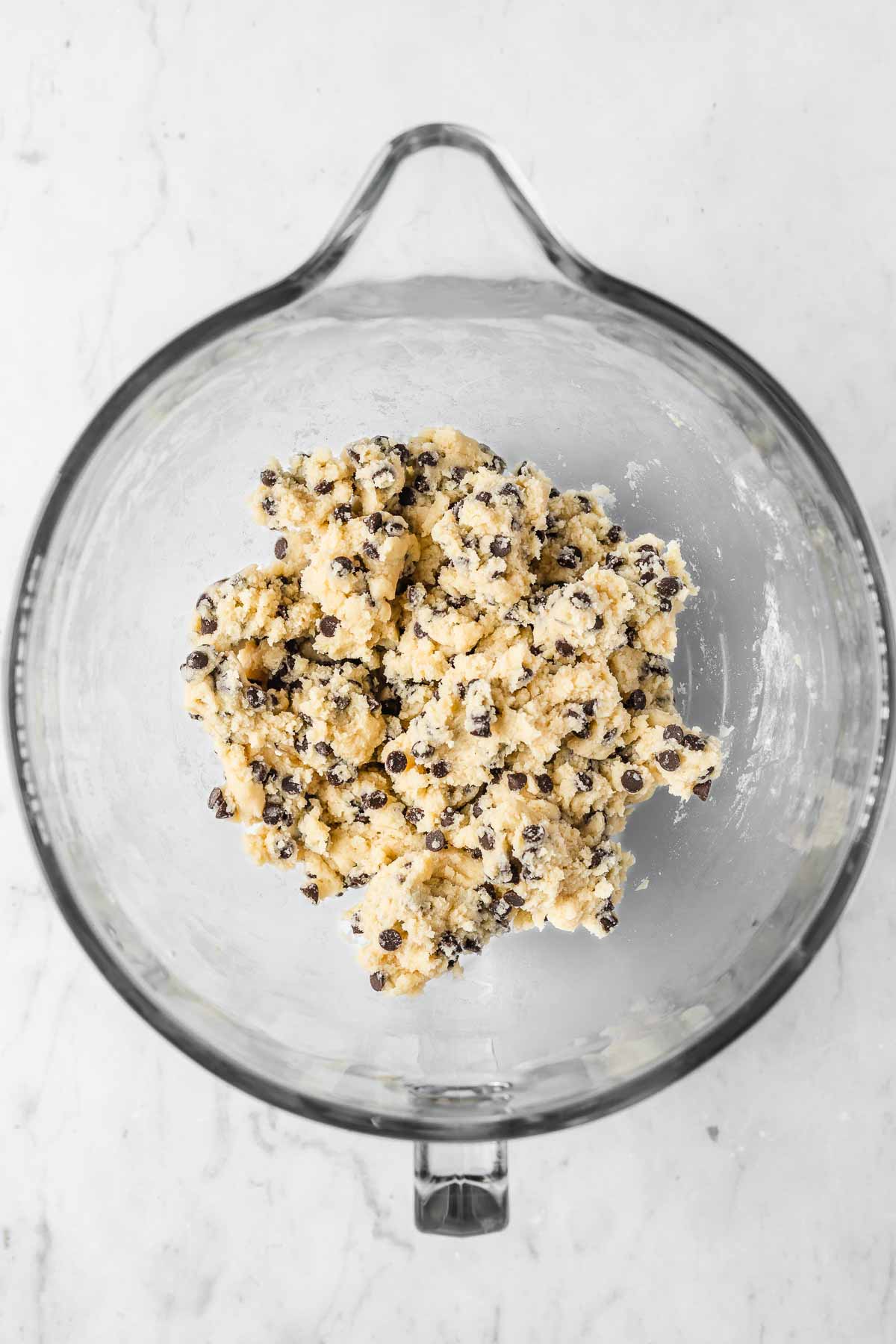 A glass mixing bowl with cookie dough inside.