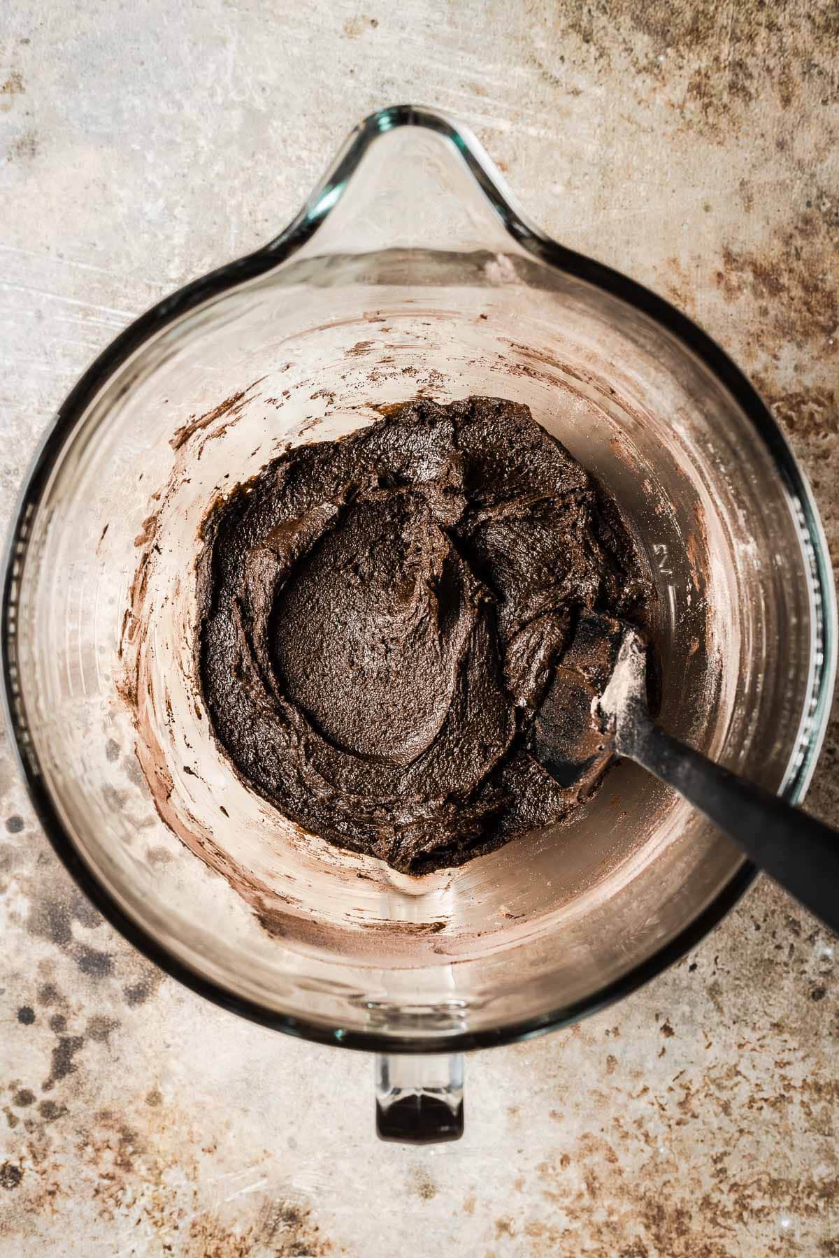 A clear mixing bowl filled with dough for chocolate cookies with dry ingredients added.