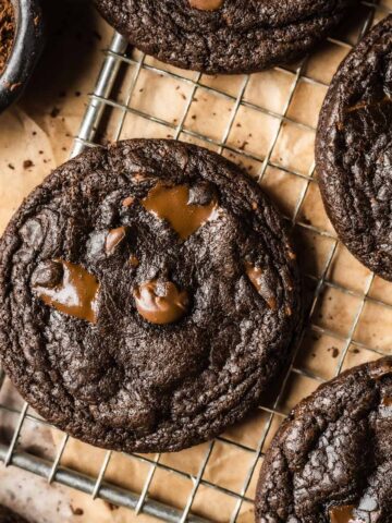 A closeup of dark brown cookies on a vintage cooling rack with brown parchment paper underneath.