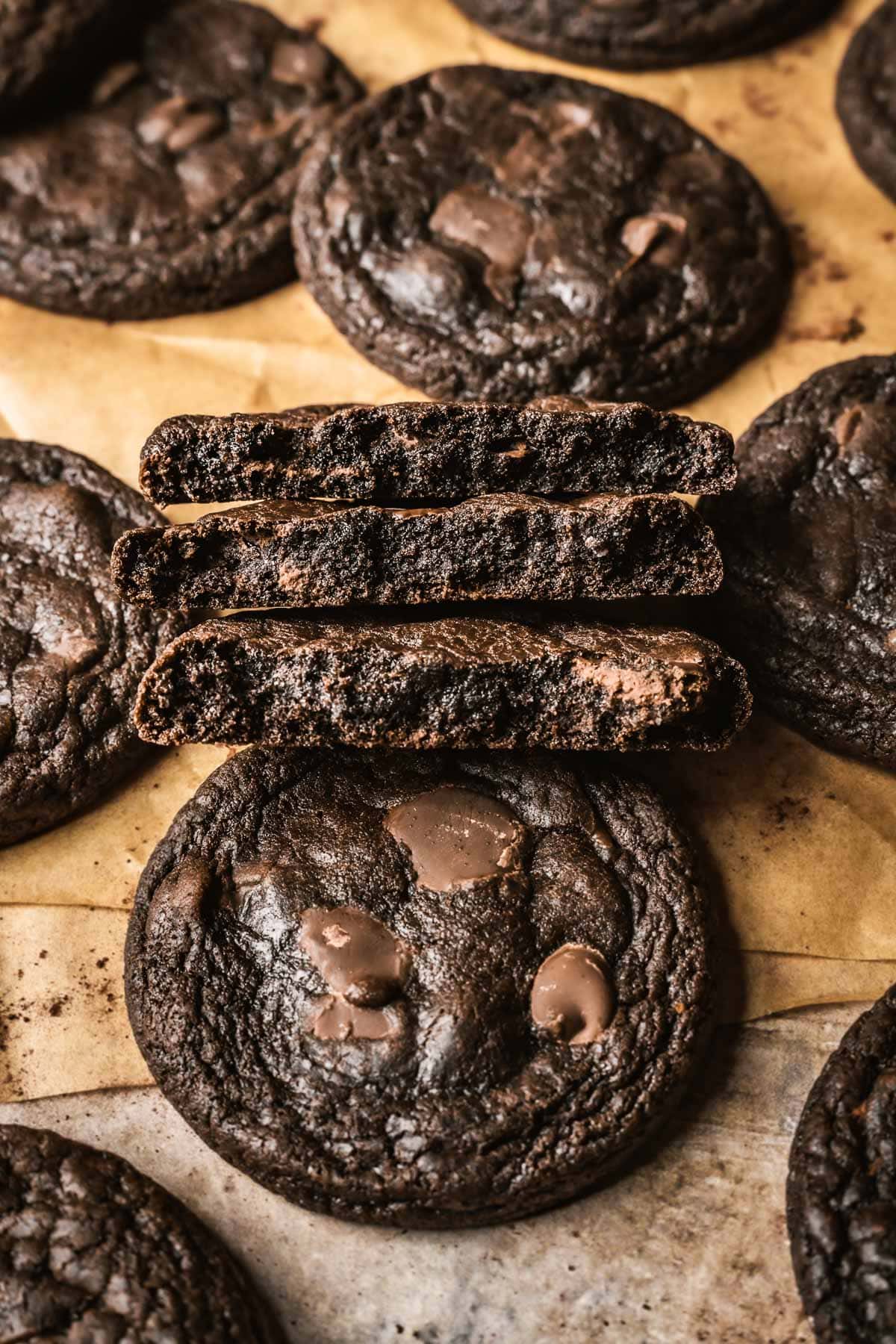 A stack of 3 cookie halves that reveal the fudgy chocolate middles of the cookies. More whole cookies surround the halves.