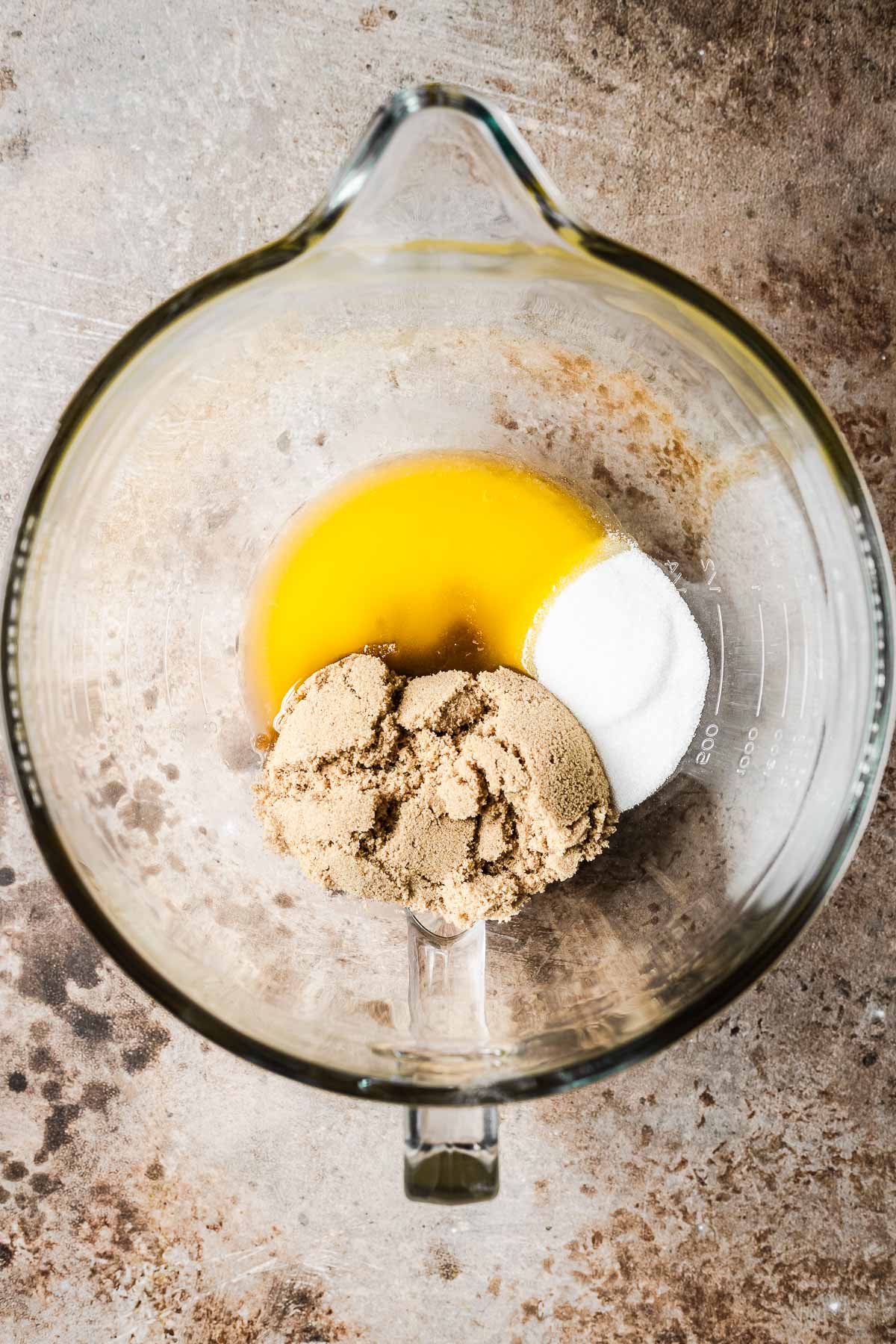 A clear mixing bowl with melted butter, brown sugar and granulated sugar inside.