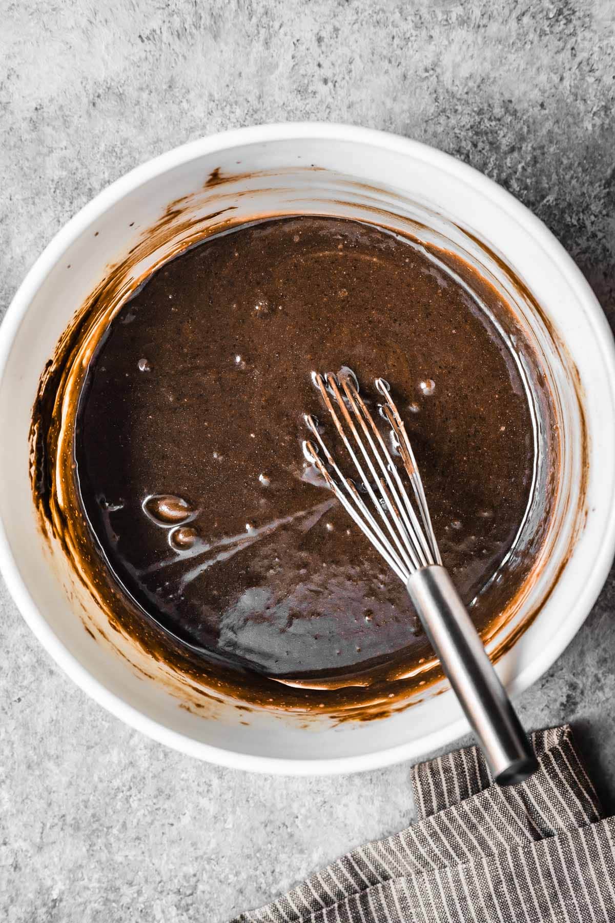 A white ceramic bowl of cake batter with eggs added.