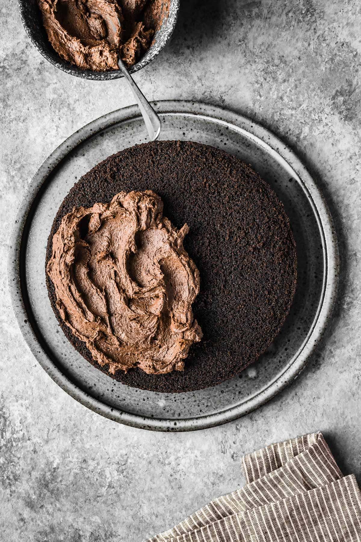 A layer of whipped ganache being spread onto a chocolate cake.