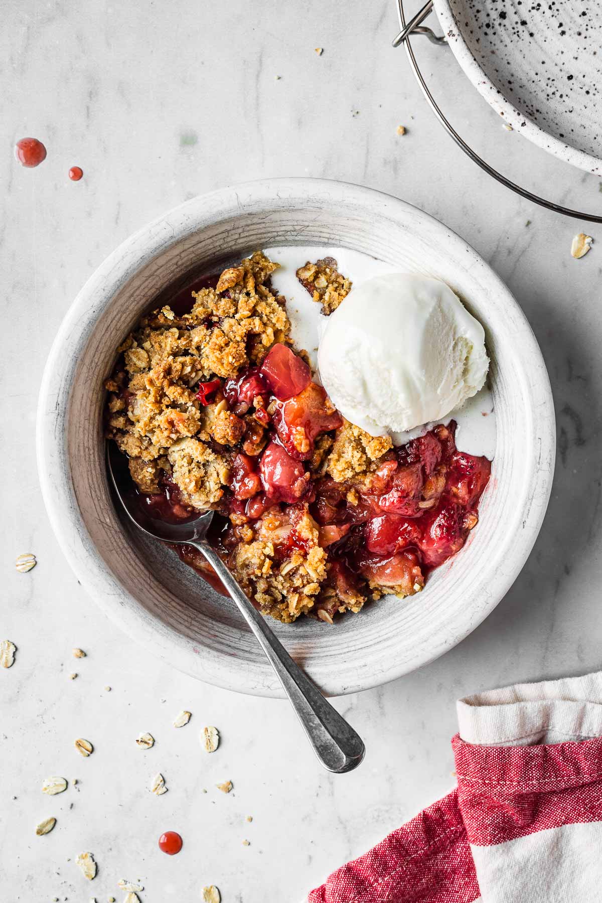 A white ceramic bowl filled with a serving of strawberry apple crisp and a scoop of vanilla ice cream.