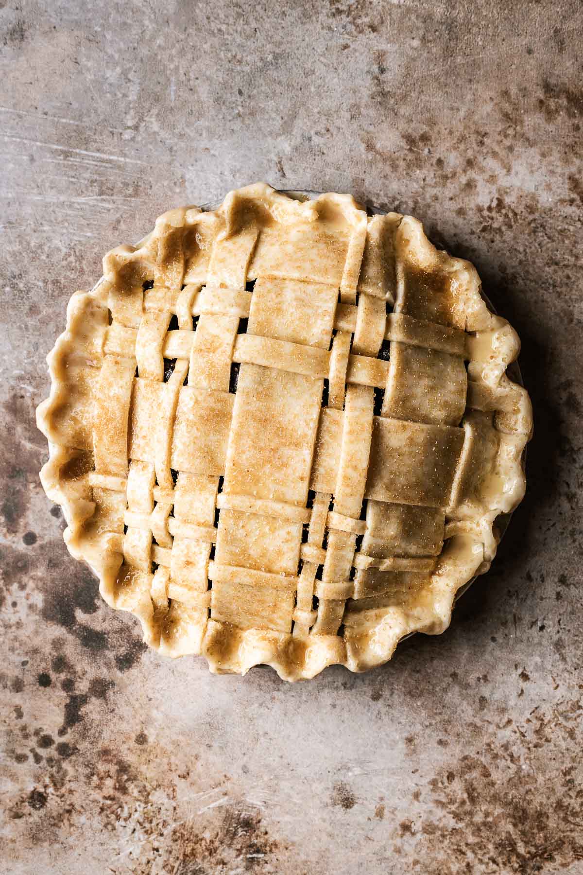 An unbaked lattice topped pie that has been brushed with egg wash and sprinkled with Turbinado sugar.