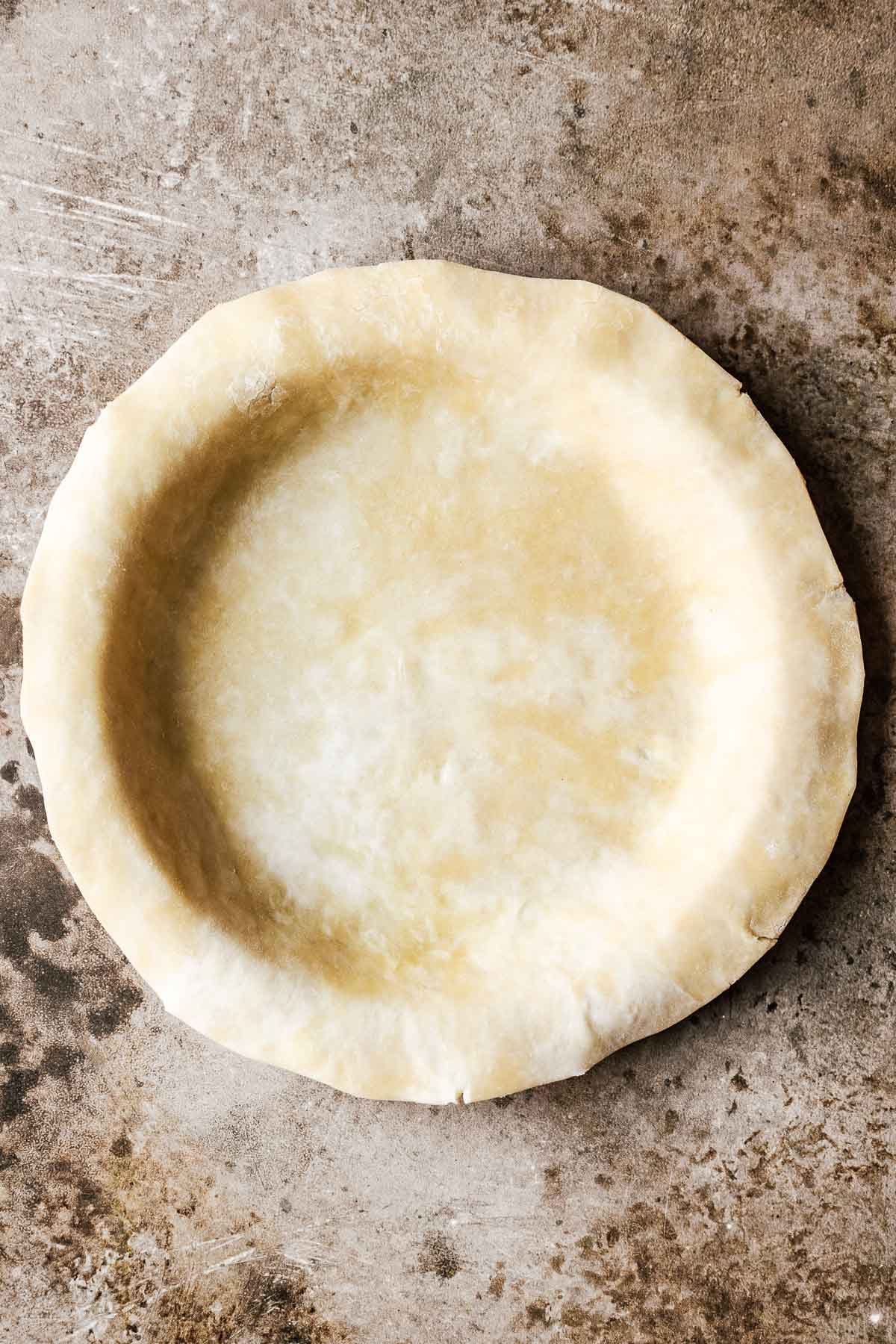 A rolled out pie crust draped over a pie pan with additional crust overlapping the edge of the pie pan.