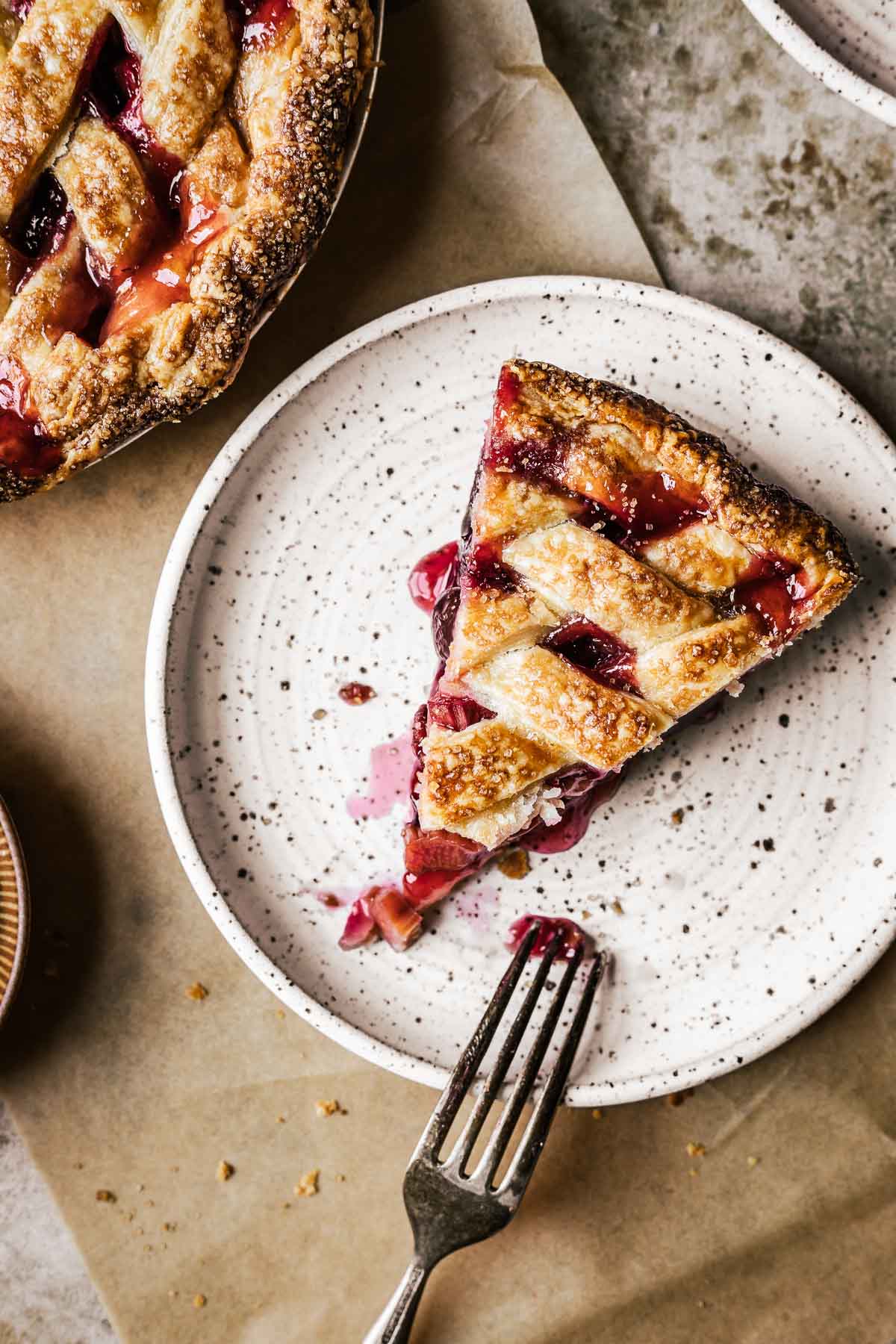 A slice of lattice topped pie on a speckled ceramic plate resting on a piece of brown parchment paper.