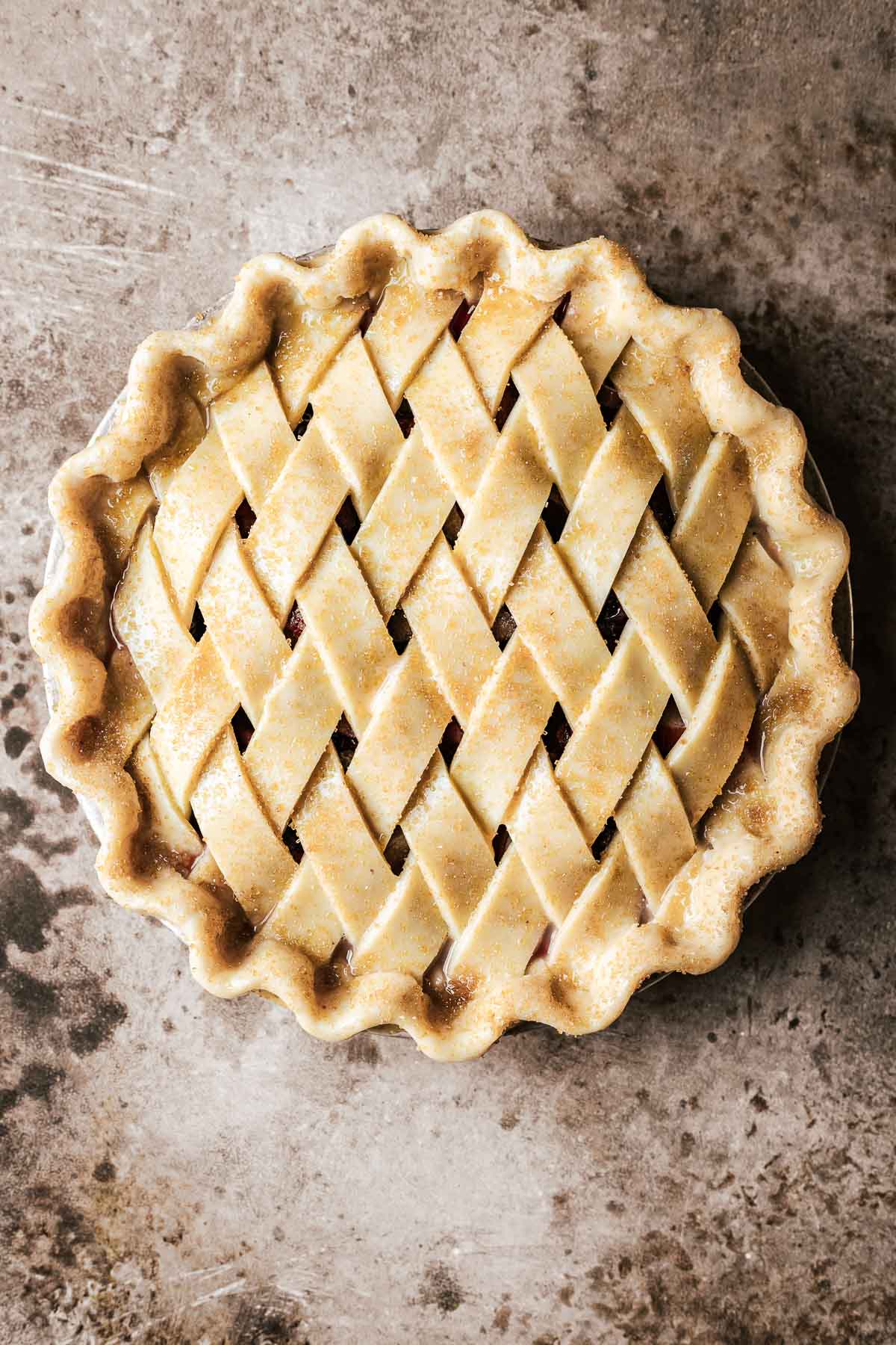 An unbaked cherry rhubarb pie with a diamond lattice and crimped edges. The crust is shiny and has been sprinkled with turbinado sugar.