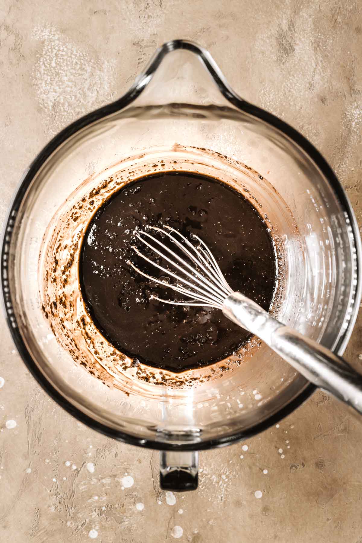 A glass mixing bowl with a mix of melted butter, cocoa powder and sugar for a cake.