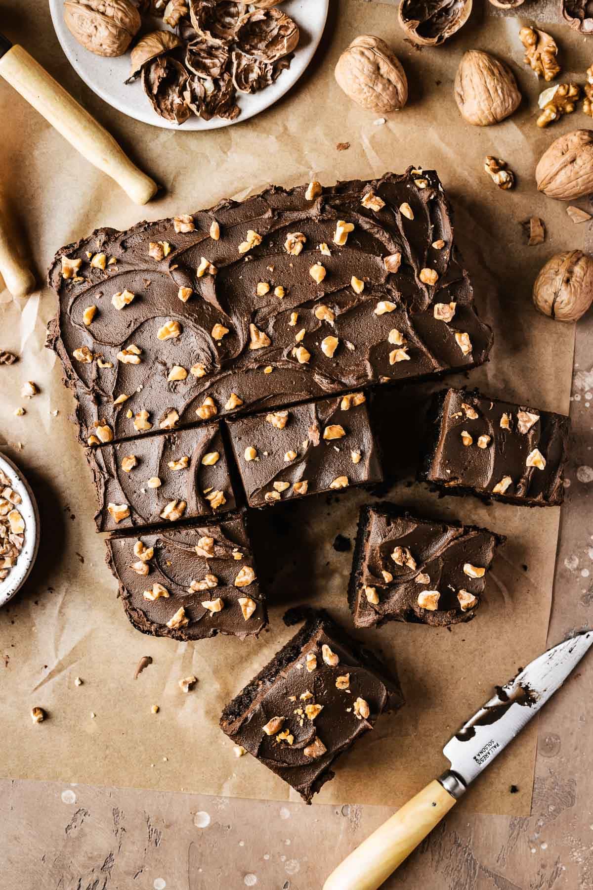 A single layer square chocolate cake on brown parchment paper with nuts sprinkled on top of the whipped chocolate ganache frosting.