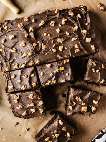 A single layer square chocolate cake on brown parchment paper with nuts sprinkled on top of whipped chocolate ganache frosting.