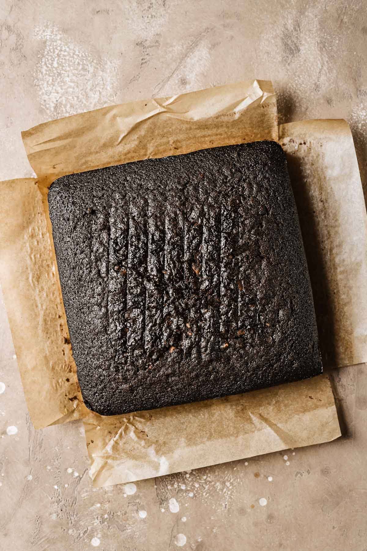 A square chocolate cake on brown parchment paper.