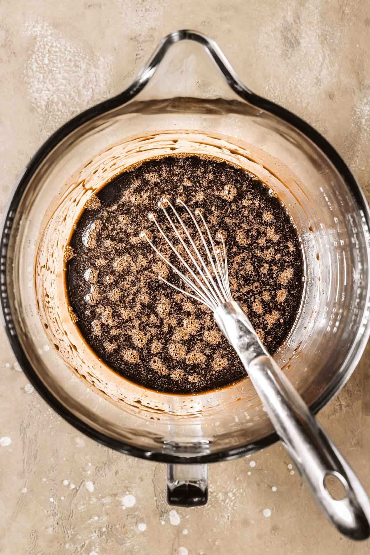 A glass mixing bowl filled with wet ingredients for cake batter.