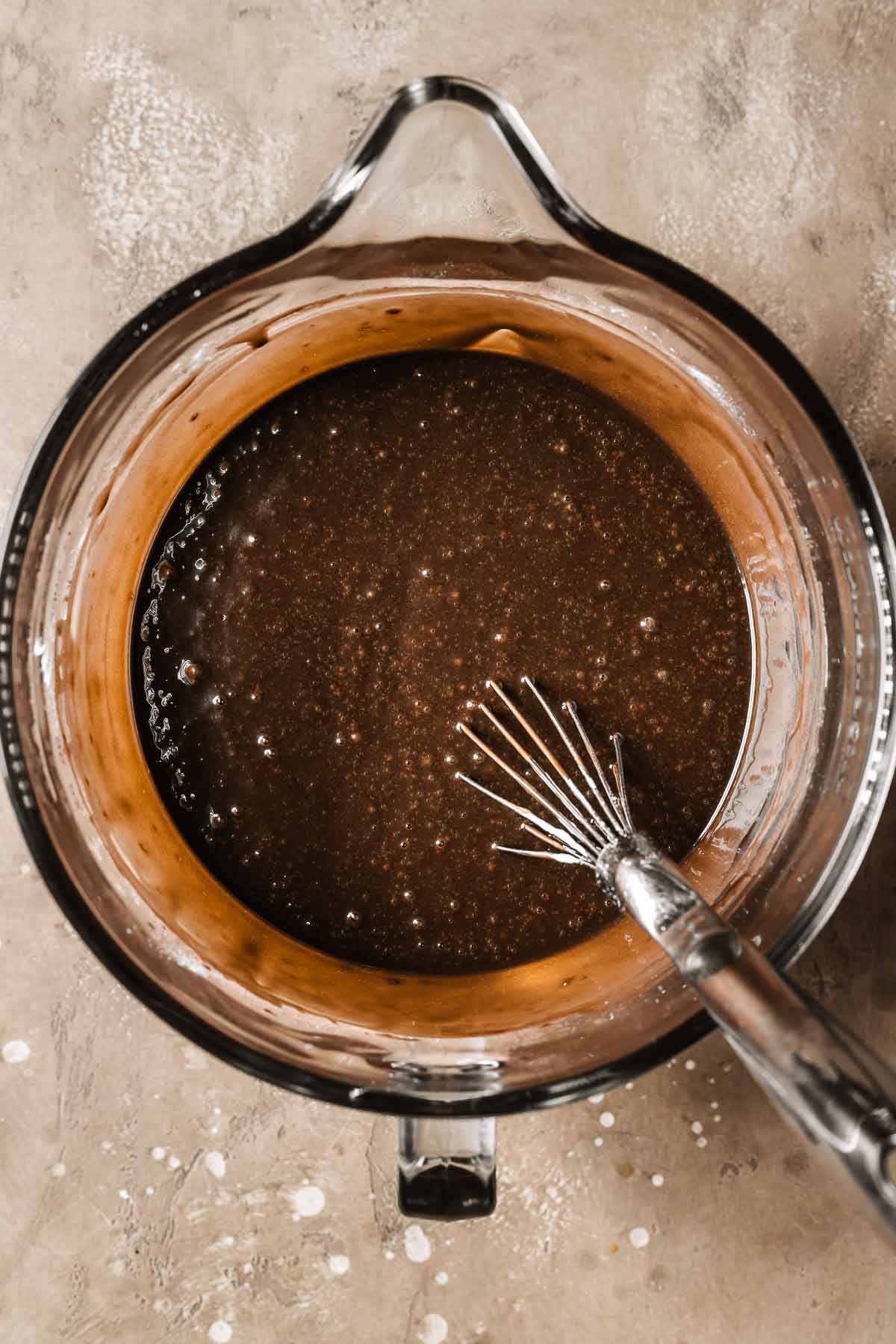 A glass mixing bowl filled with chocolate cake batter.