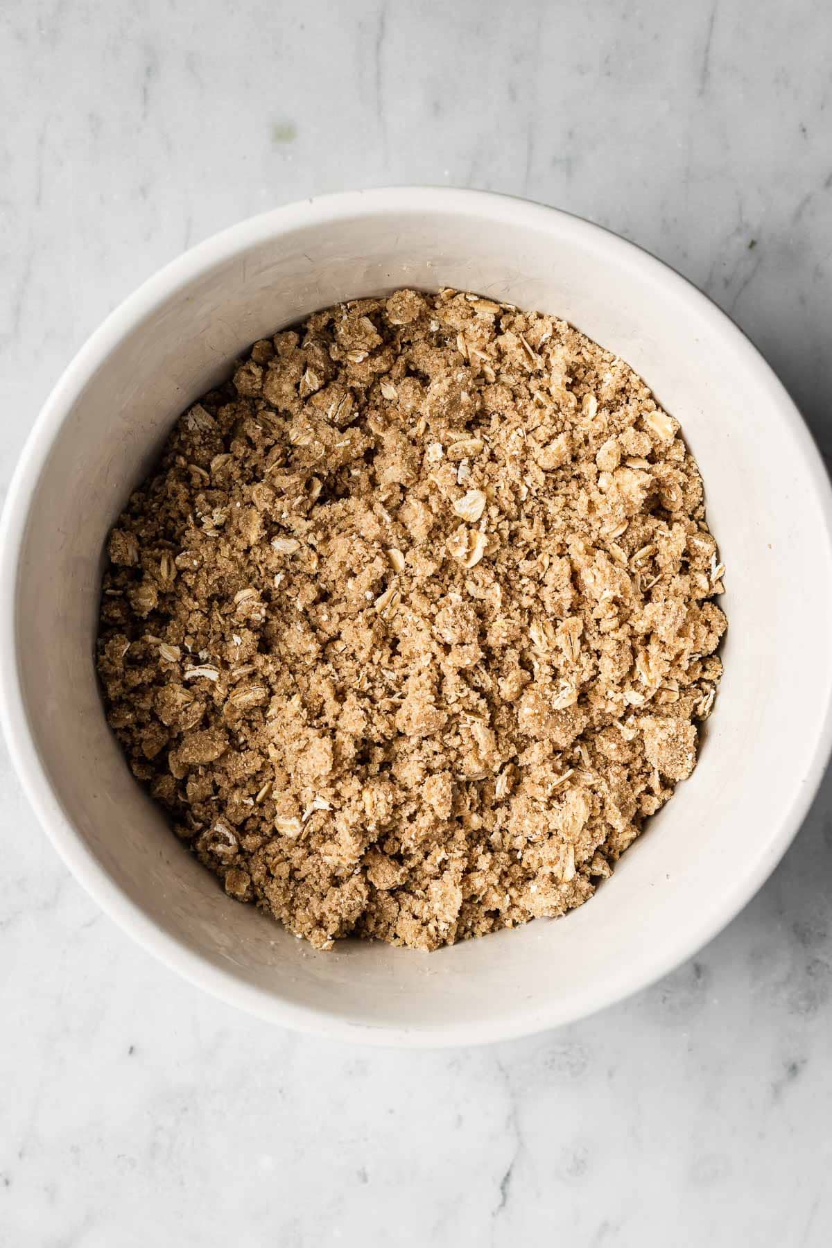 A white ceramic bowl filled with topping for a fruit crisp.