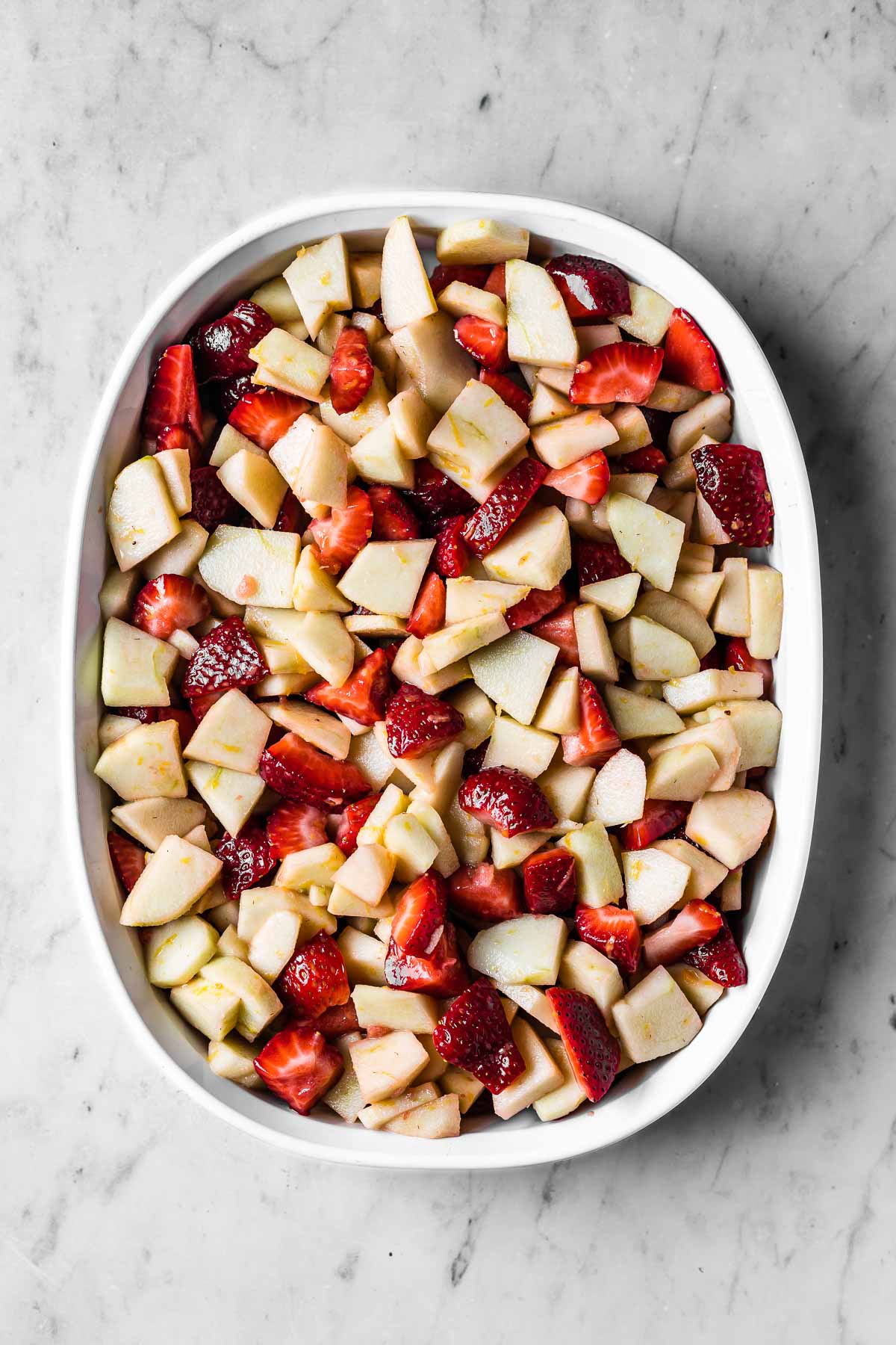 A white ceramic baking dish full of unbaked strawberry apple crisp filling.