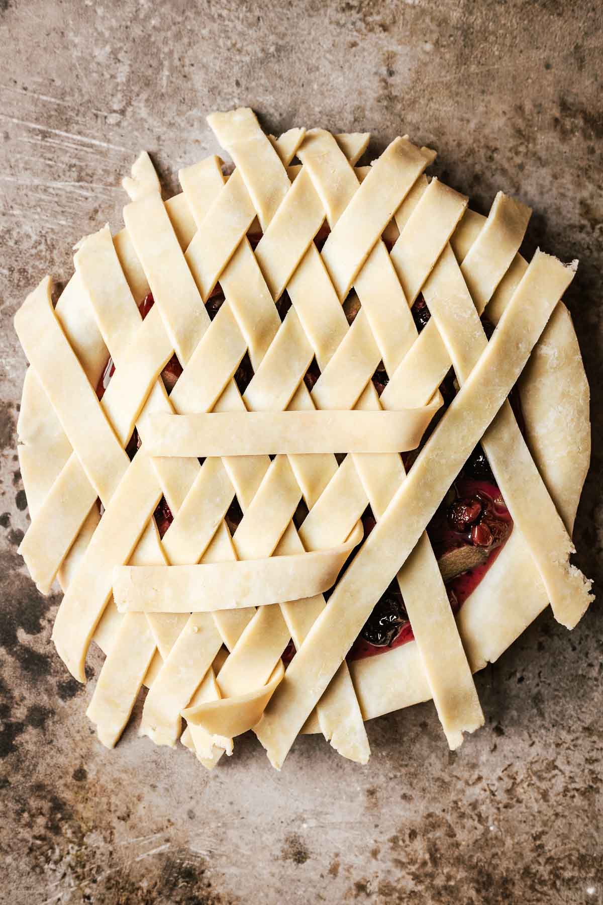 A filled cherry rhubarb pie with lattice pieces being woven on top.