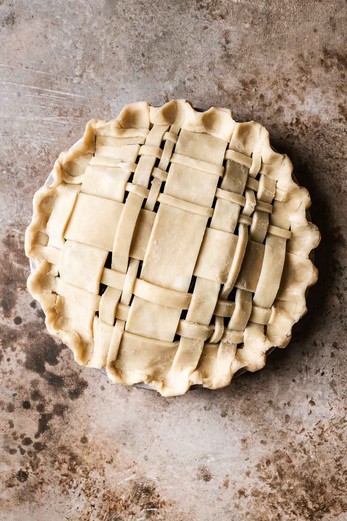 An unbaked, lattice topped, crimped edge blueberry pie with frozen blueberries.