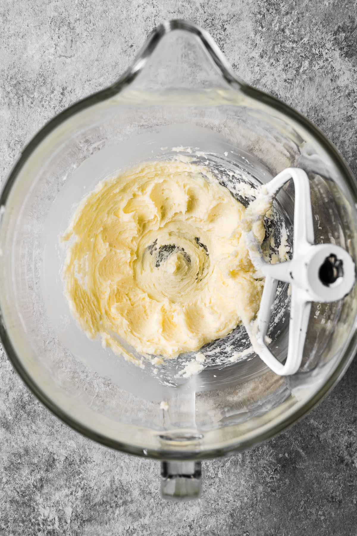 A glass mixing bowl with creamed butter and sugar.