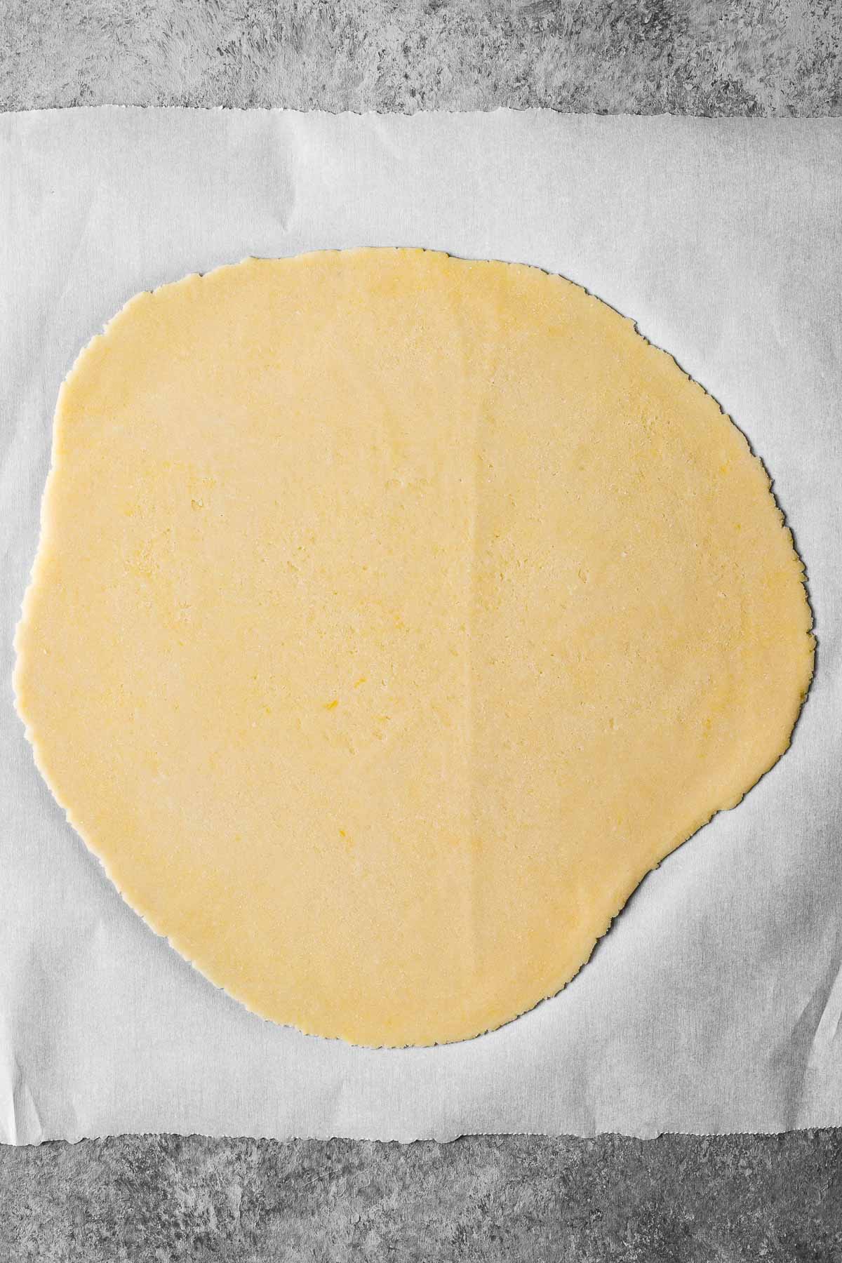 Pate sucree dough rolled out into a rough circle on a piece of white parchment paper.