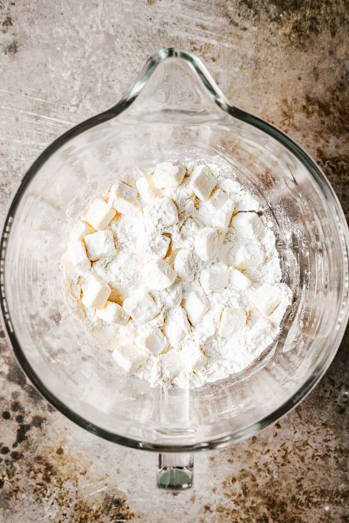 A glass mixing bowl filled with flour, salt and cubed butter for pie crust.