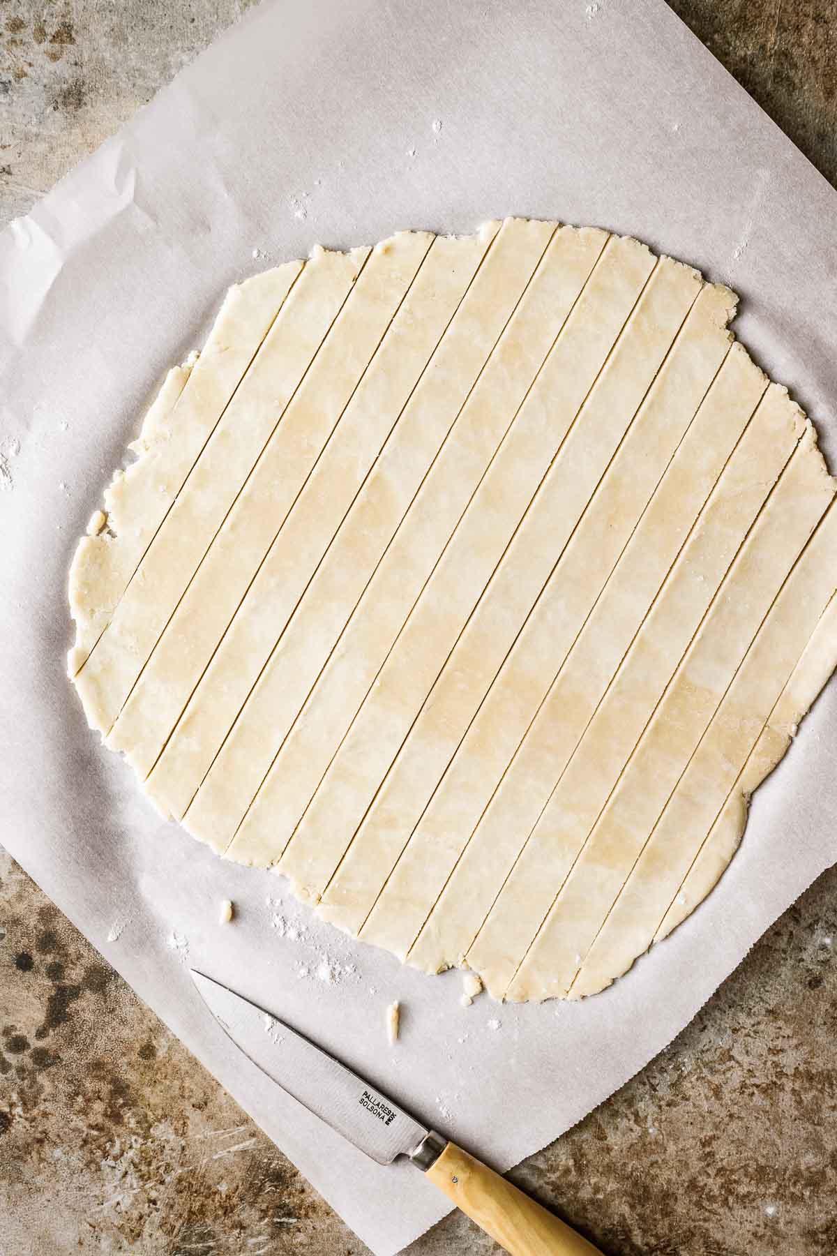 White parchment paper with pie dough on top that has been cut into even strips for lattice.
