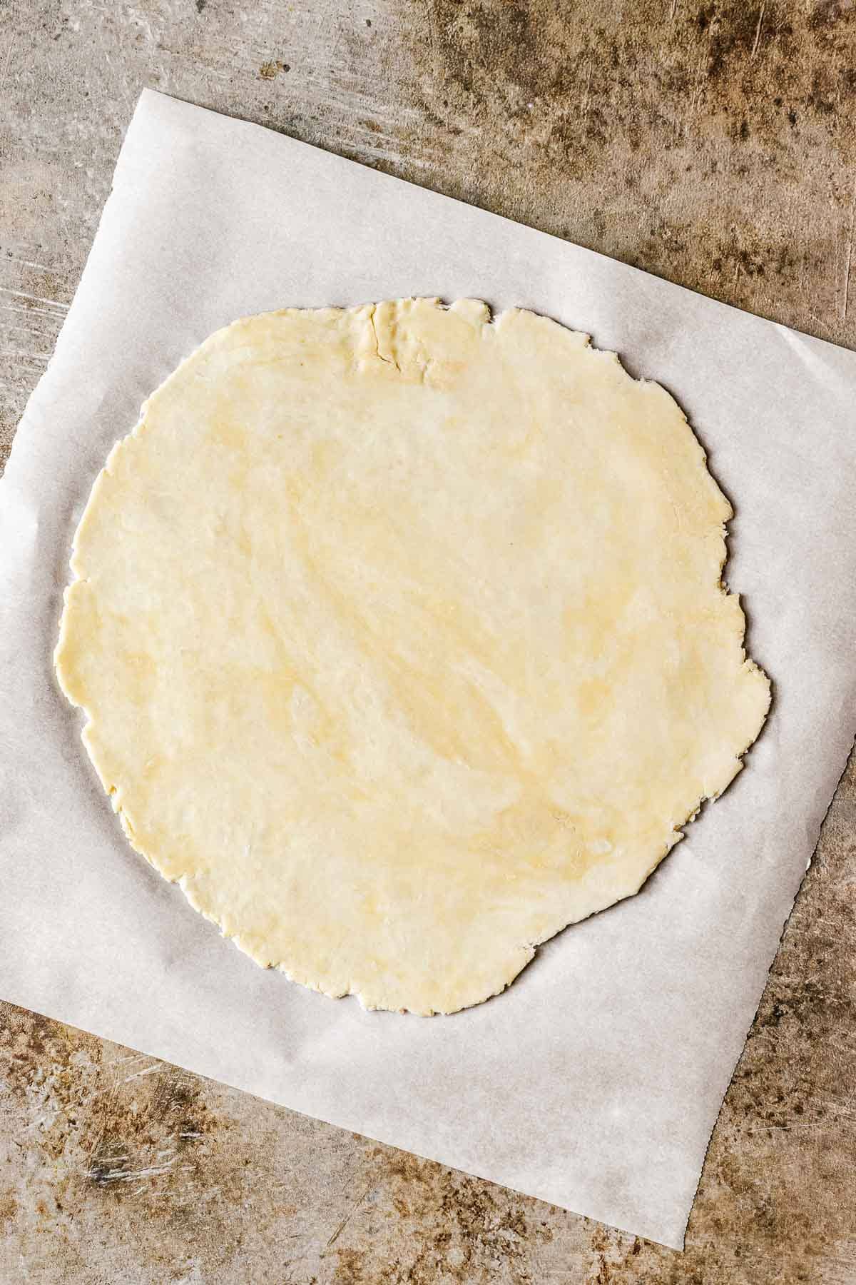 Pie dough rolled into a circle on a piece of white parchment paper.