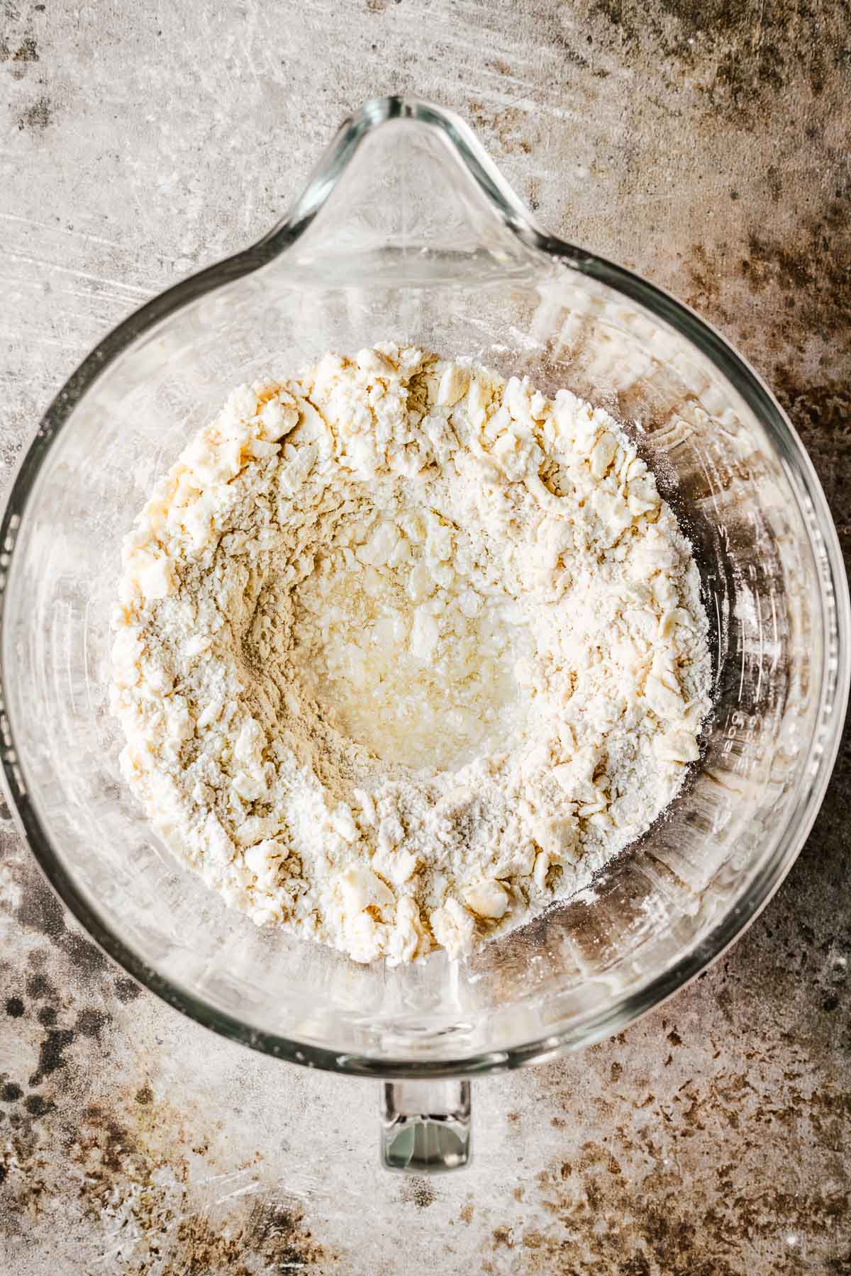 A glass mixing bowl with wet ingredients in a well in the middle of dry ingredients and cut-in butter.