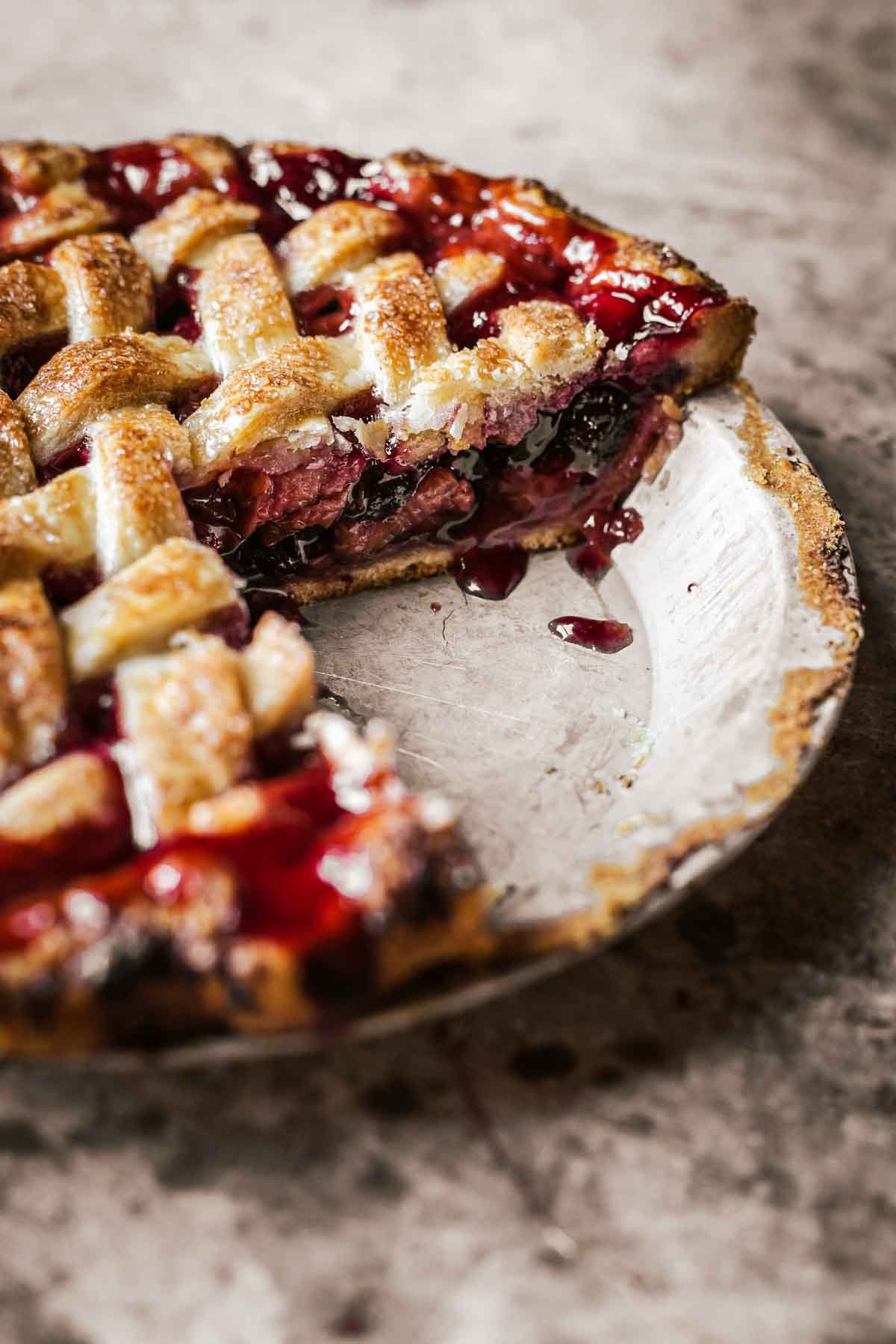 A cherry rhubarb pie in a vintage pie pan with a slice removed, revealing the side view of the sliced pie.
