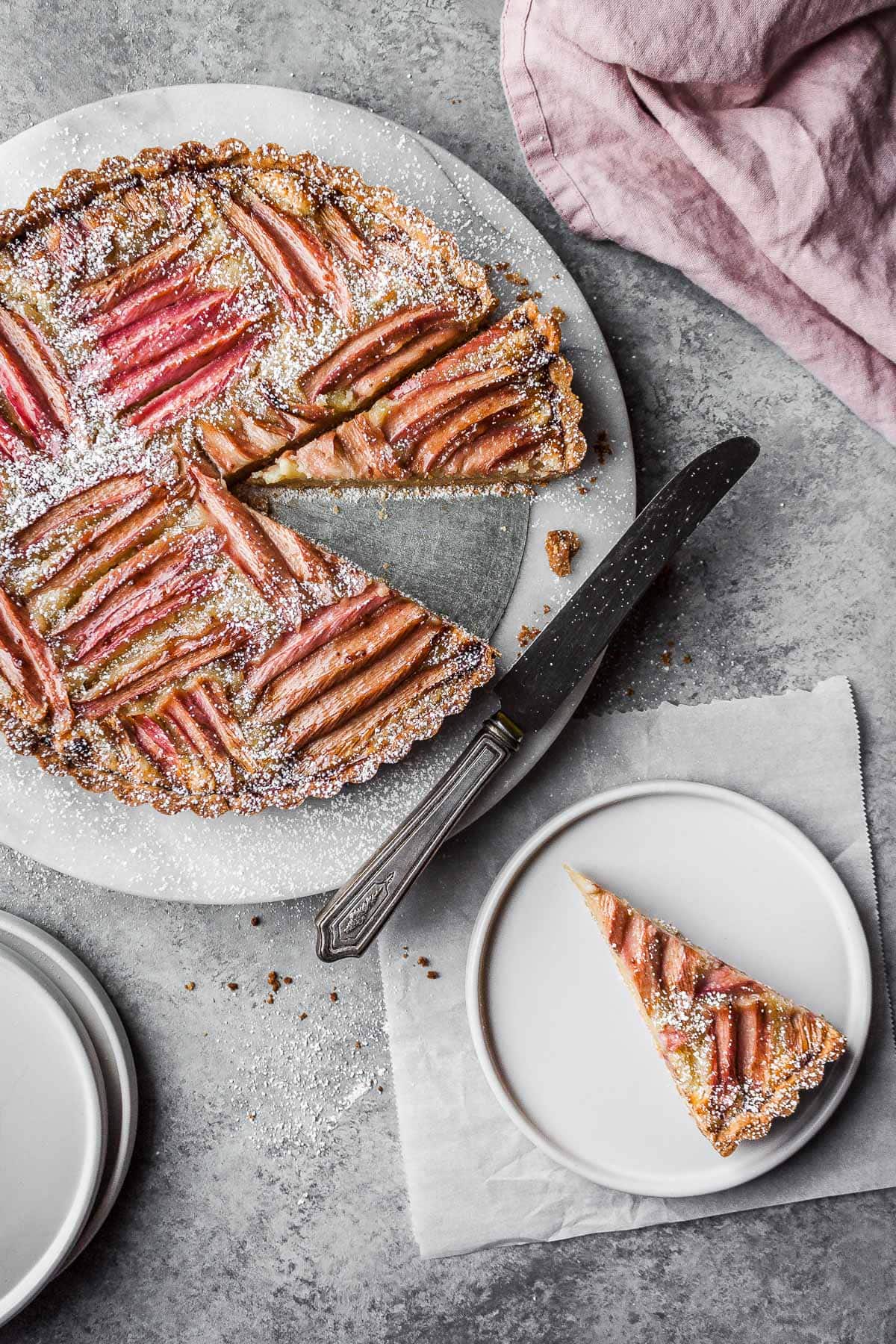 Rhubarb tart with a slice on a white plate nearby.