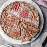 Rhubarb frangipane tart on a round marble platter with two slices cut.