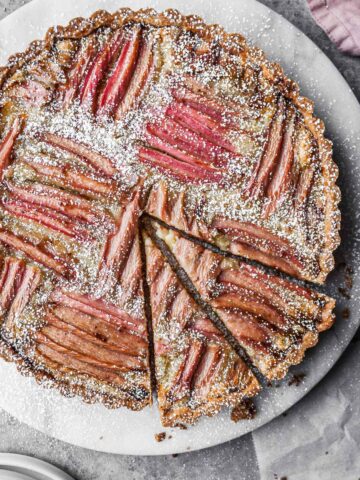 Rhubarb frangipane tart on a round marble platter with two slices cut.
