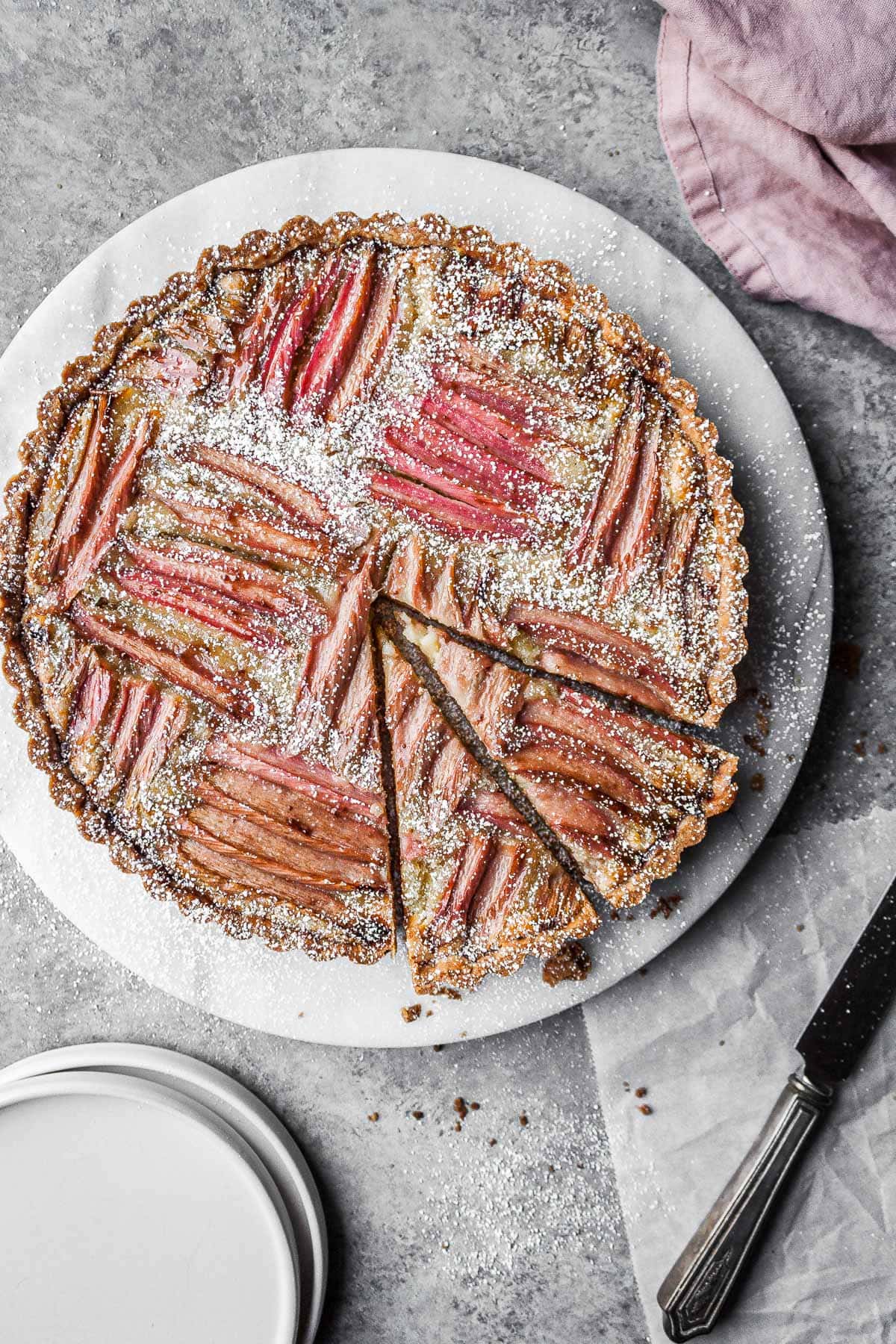 Rhubarb frangipane tart on a round marble platter with two slices cut.