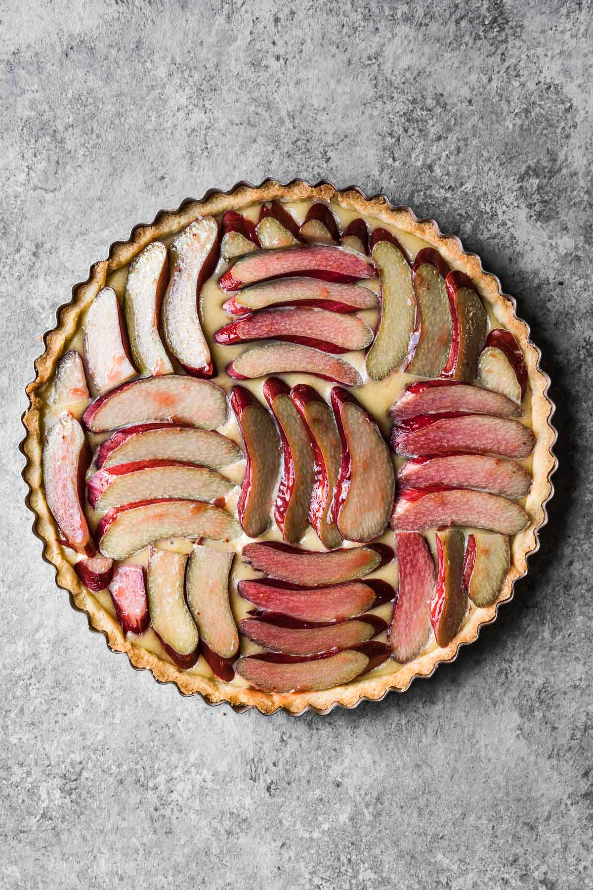 Unbaked tart filled with frangipane and topped with sliced rhubarb arranged in a parquet pattern.