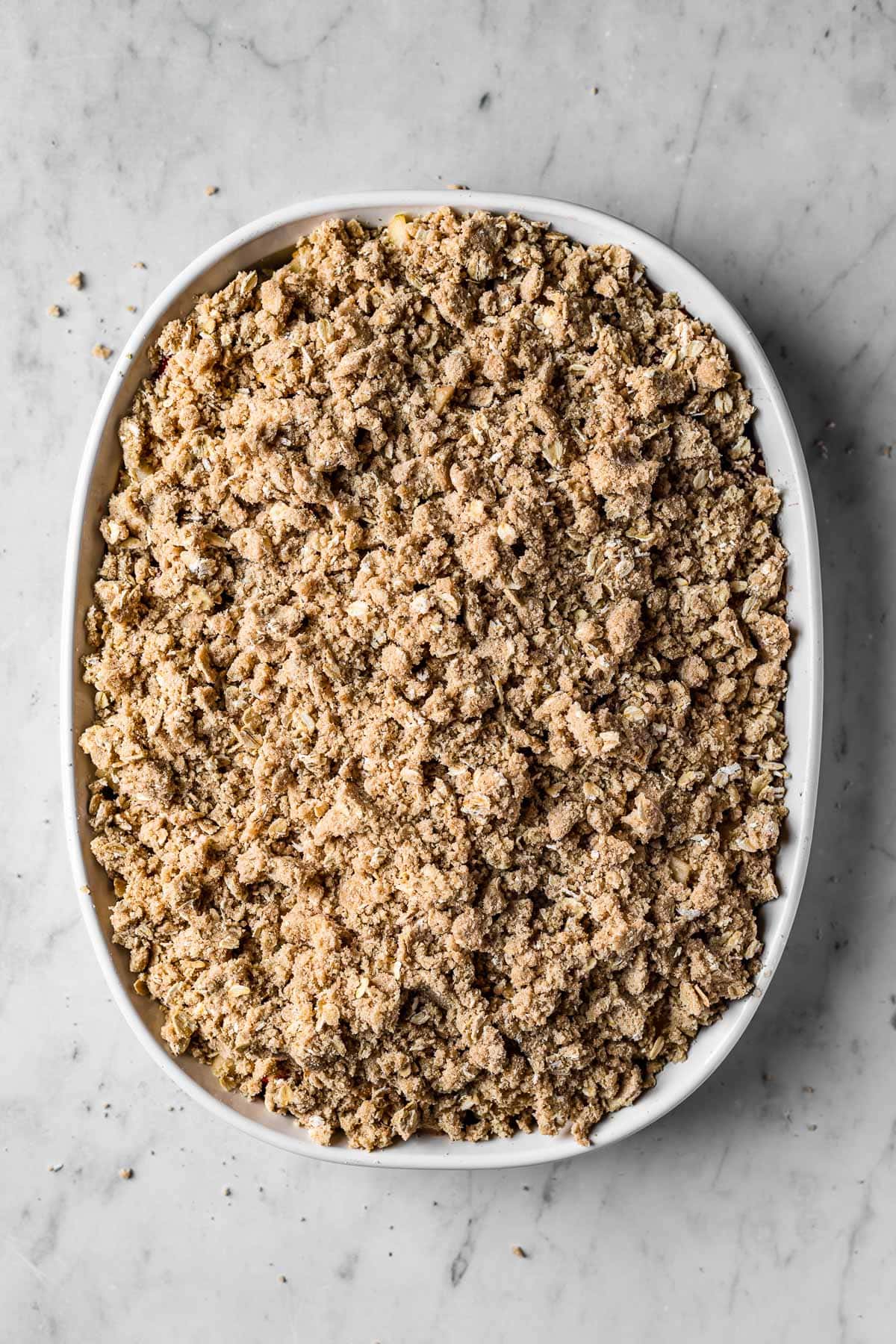 A white ceramic baking dish filled with an unbaked fruit crisp covered with topping.