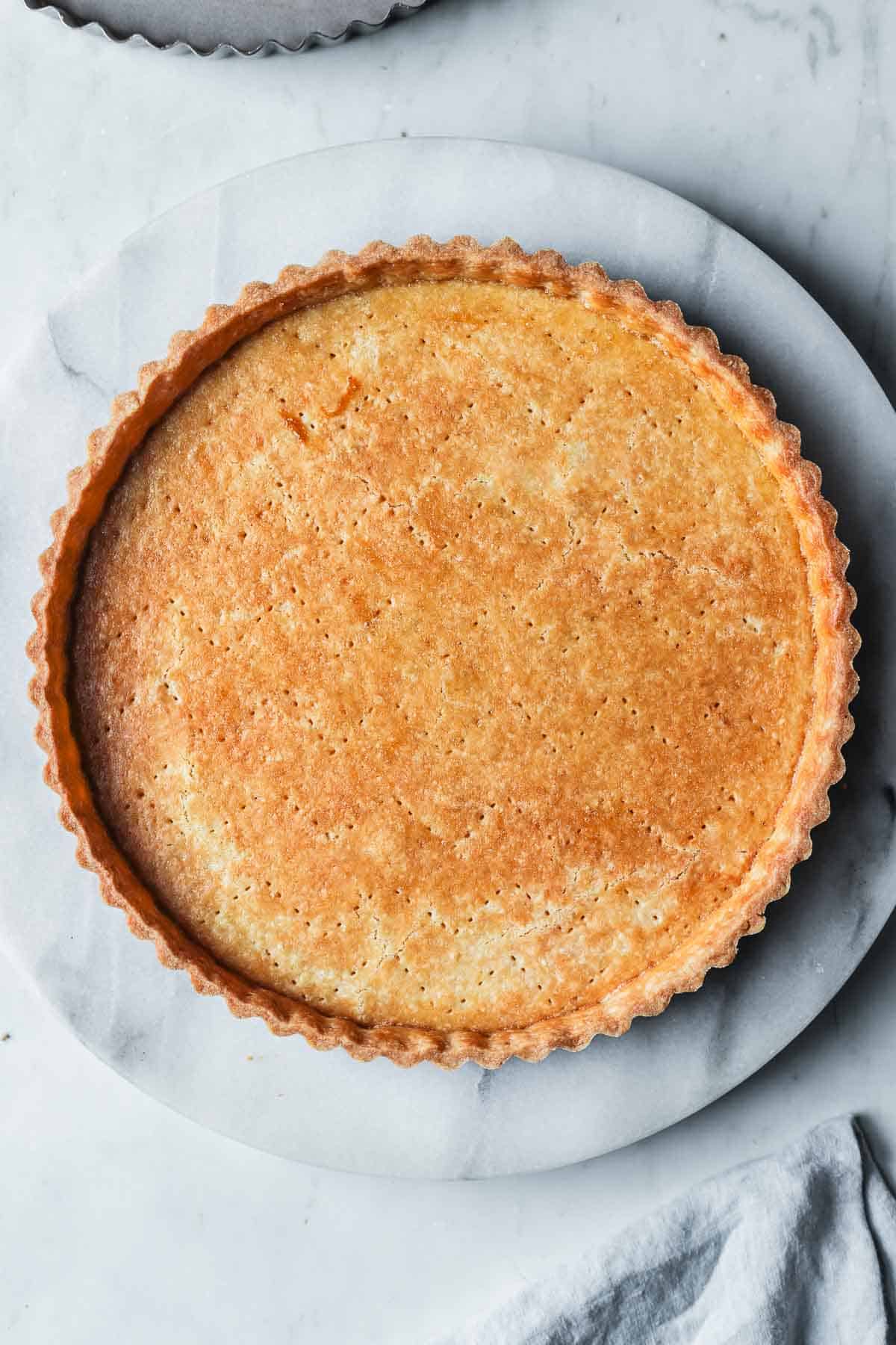 A golden brown baked pate sucree tart shell on a marble platter.