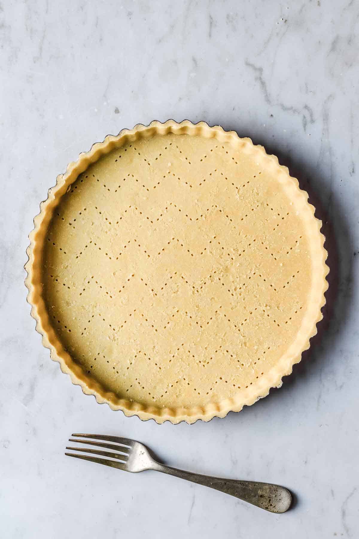 Tart dough in pan that has been docked with a fork in a chevron pattern.